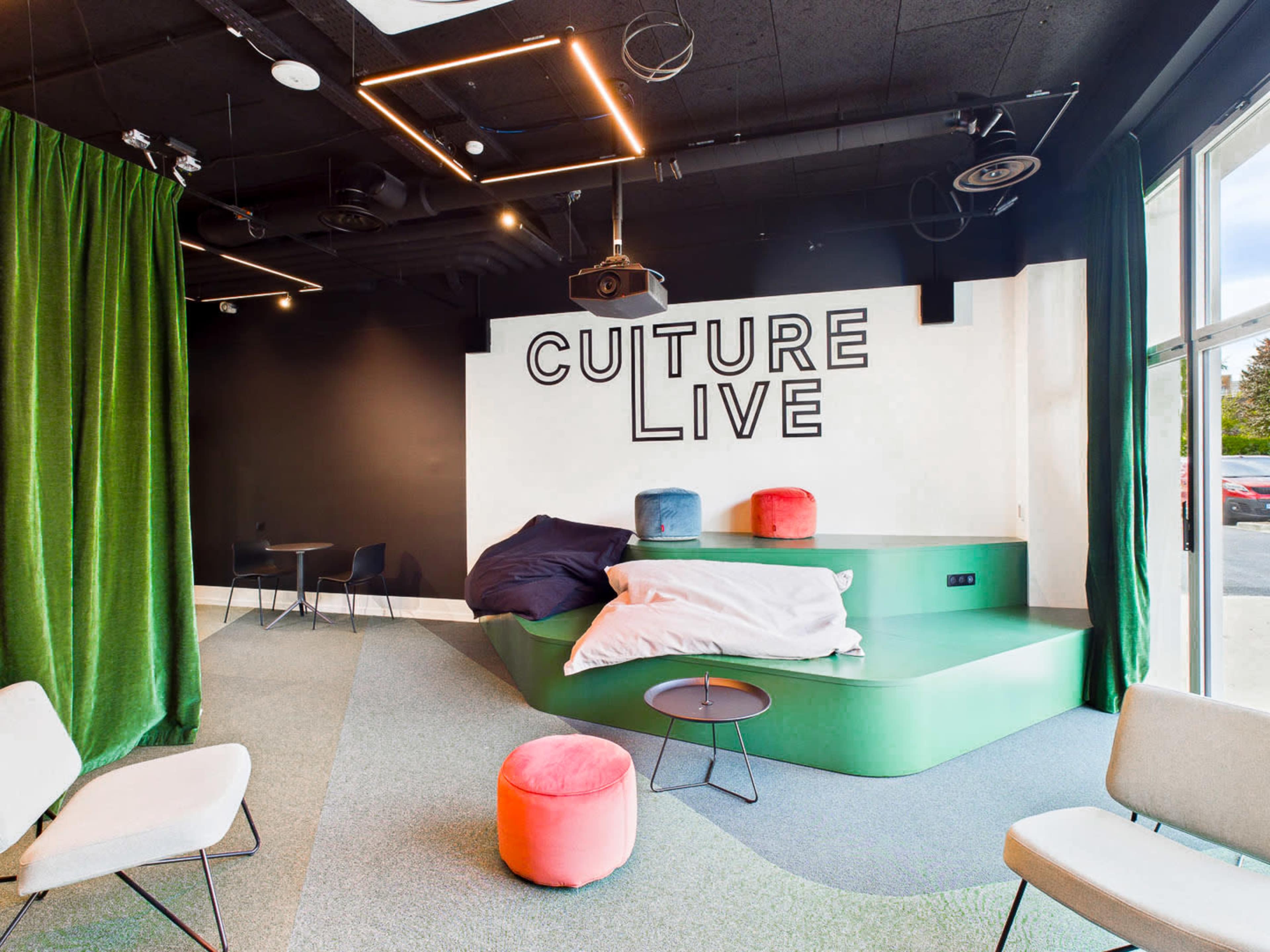 The image shows a modern lounge area with green seating, colorful poufs, and a large "CULTURE LIVE" sign on the wall.