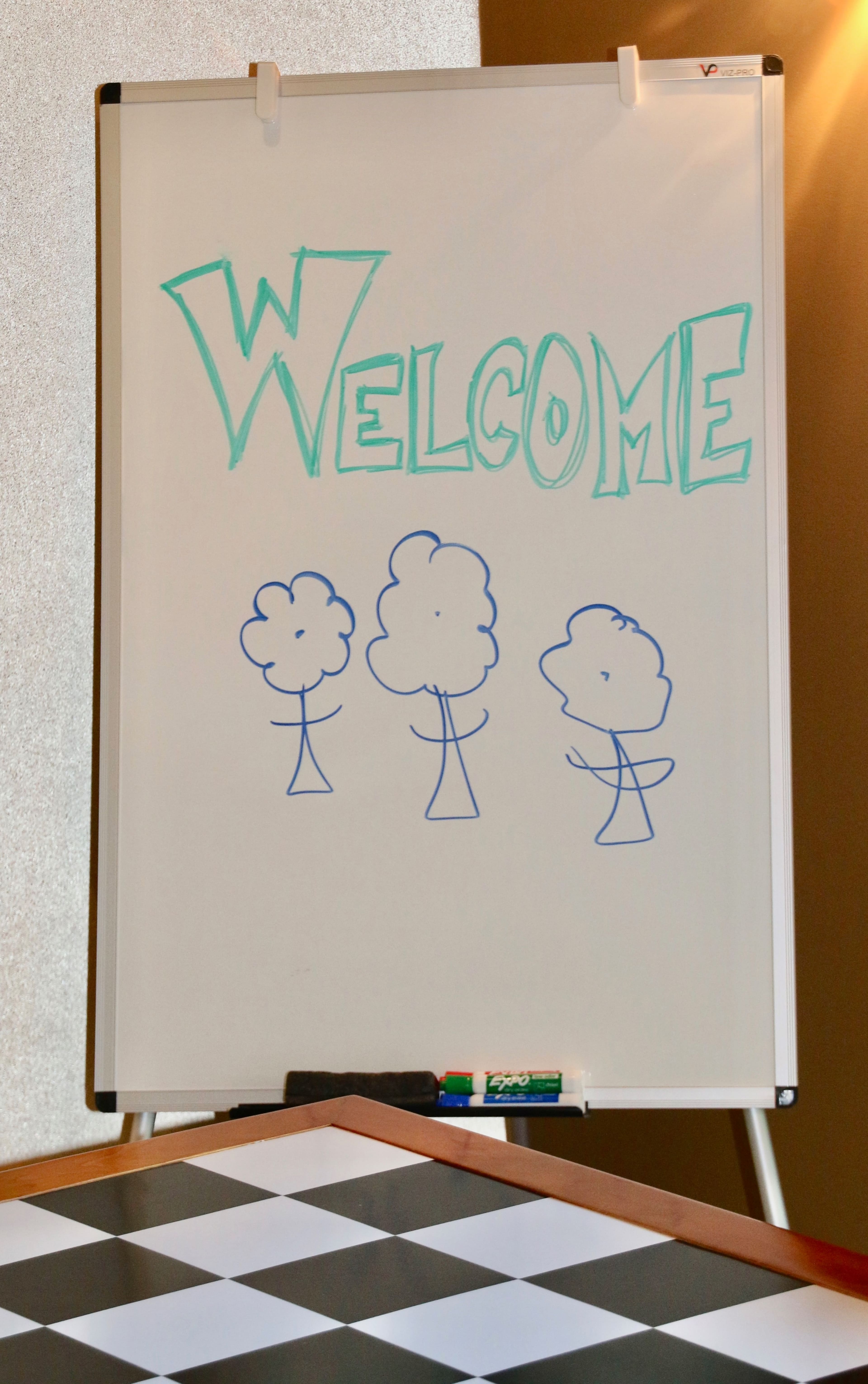 A whiteboard displays the word "WELCOME" above three simple tree drawings.