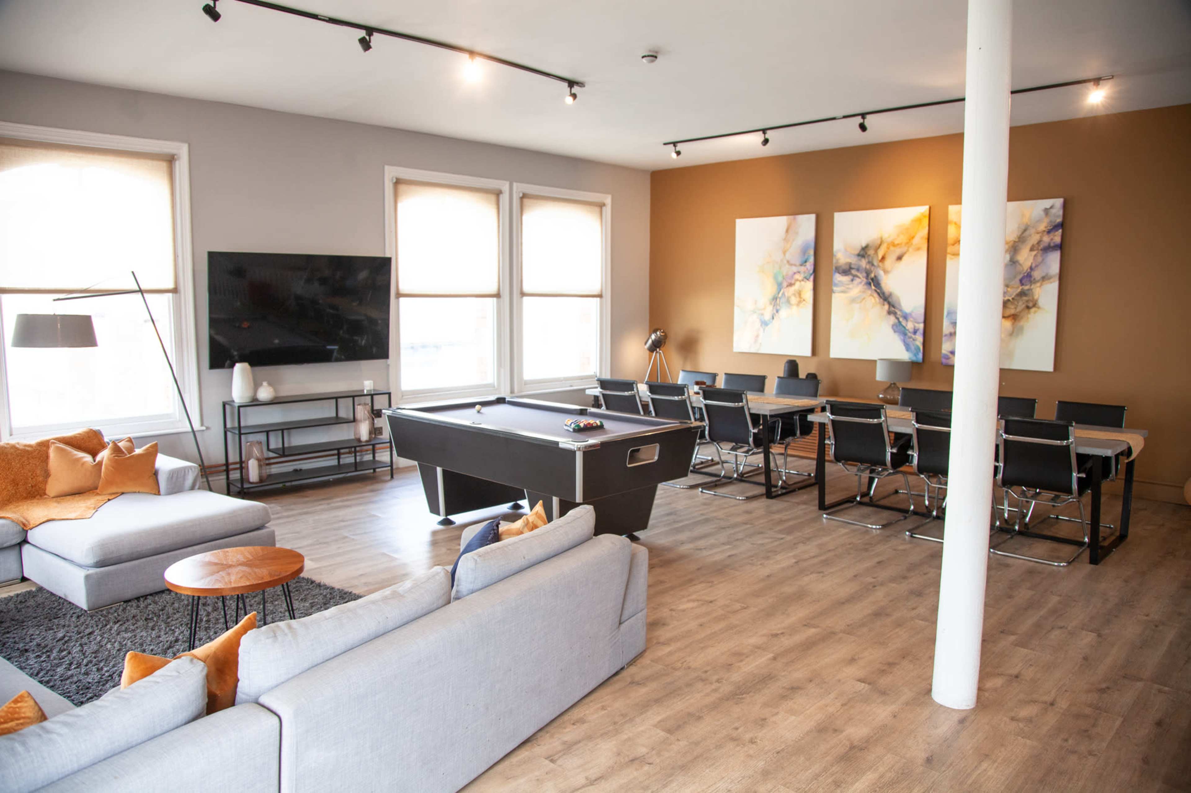 The image shows a spacious living area featuring a pool table, a large seating arrangement, a dining table, and abstract artwork on the walls.
