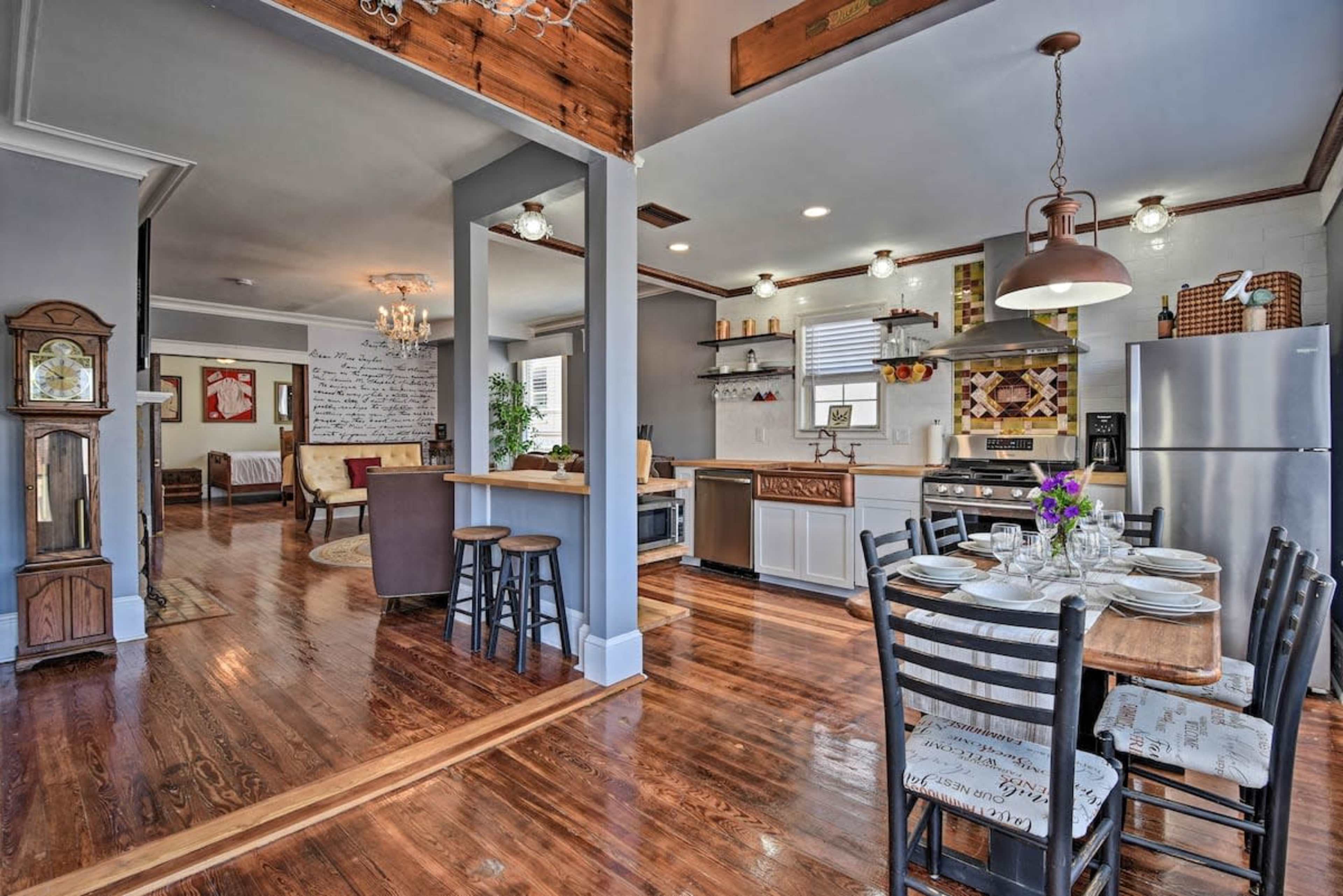 The image features a modern kitchen and dining area with wooden flooring, a dining table set for six, and stainless steel appliances.