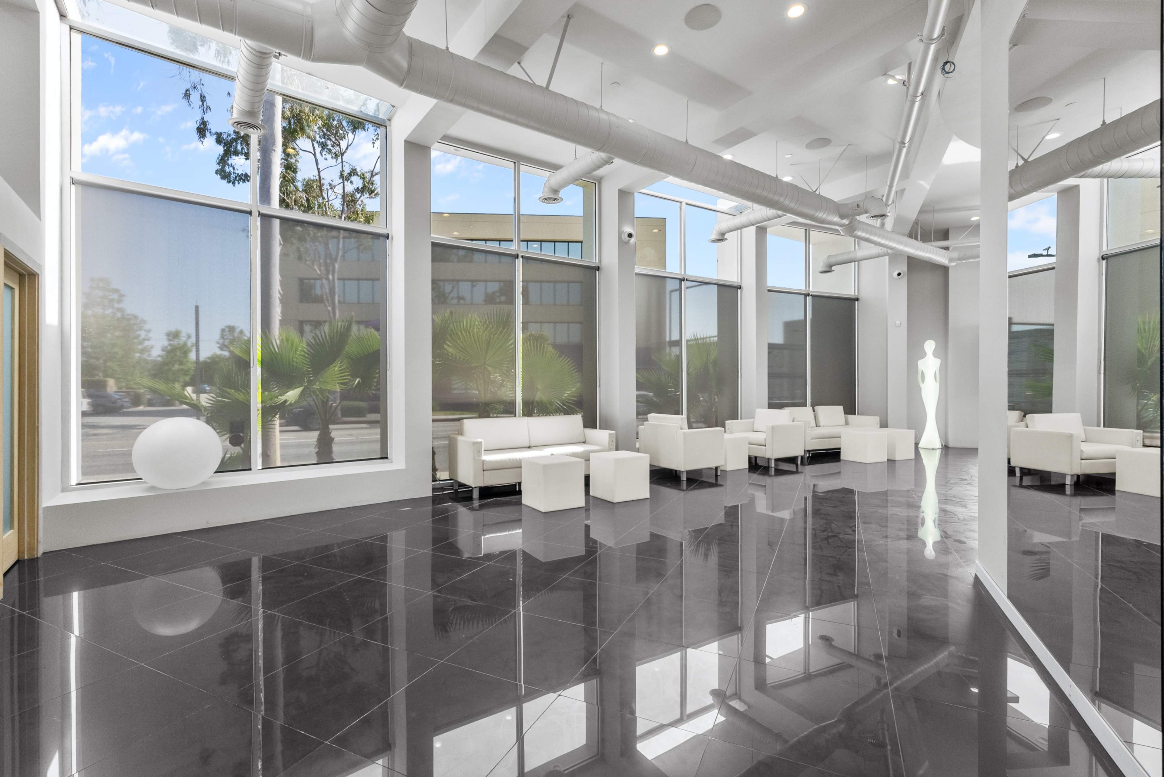 The image shows a modern lobby with glossy black flooring, large windows, and white furniture arranged in an open layout.
