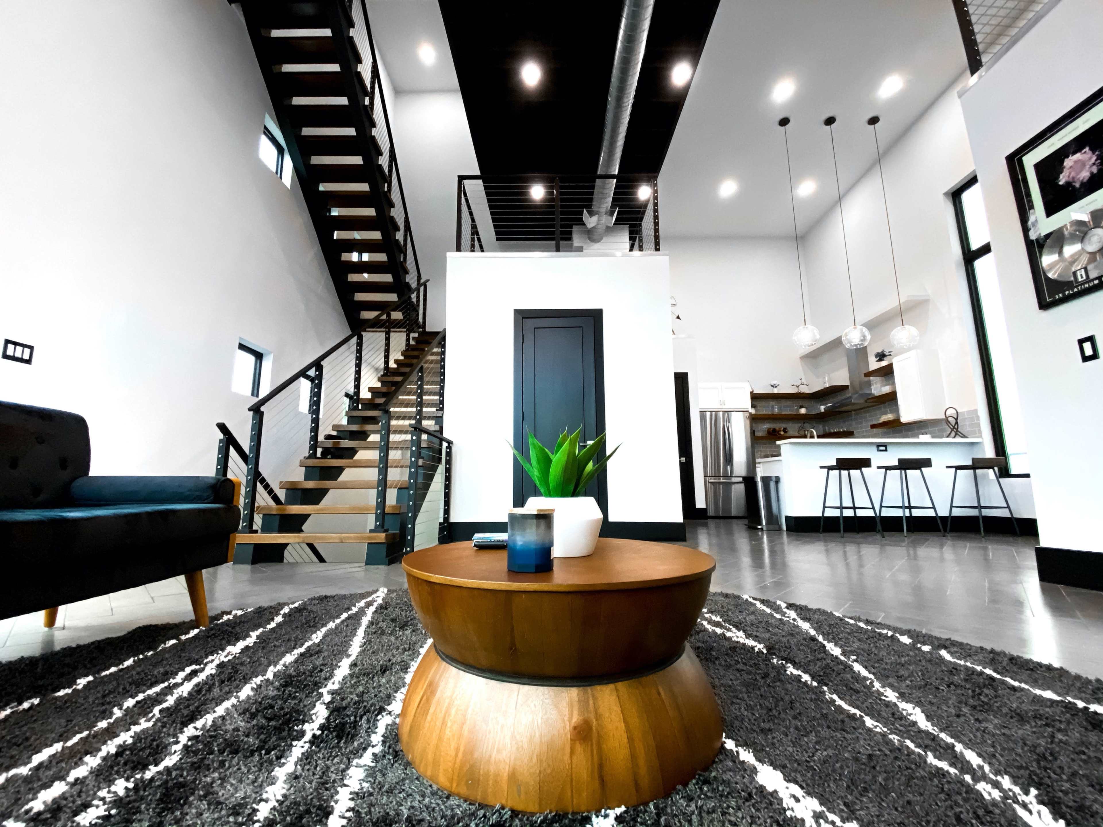 A modern living area with a wooden coffee table, a green plant, and a staircase leading to an upper level.