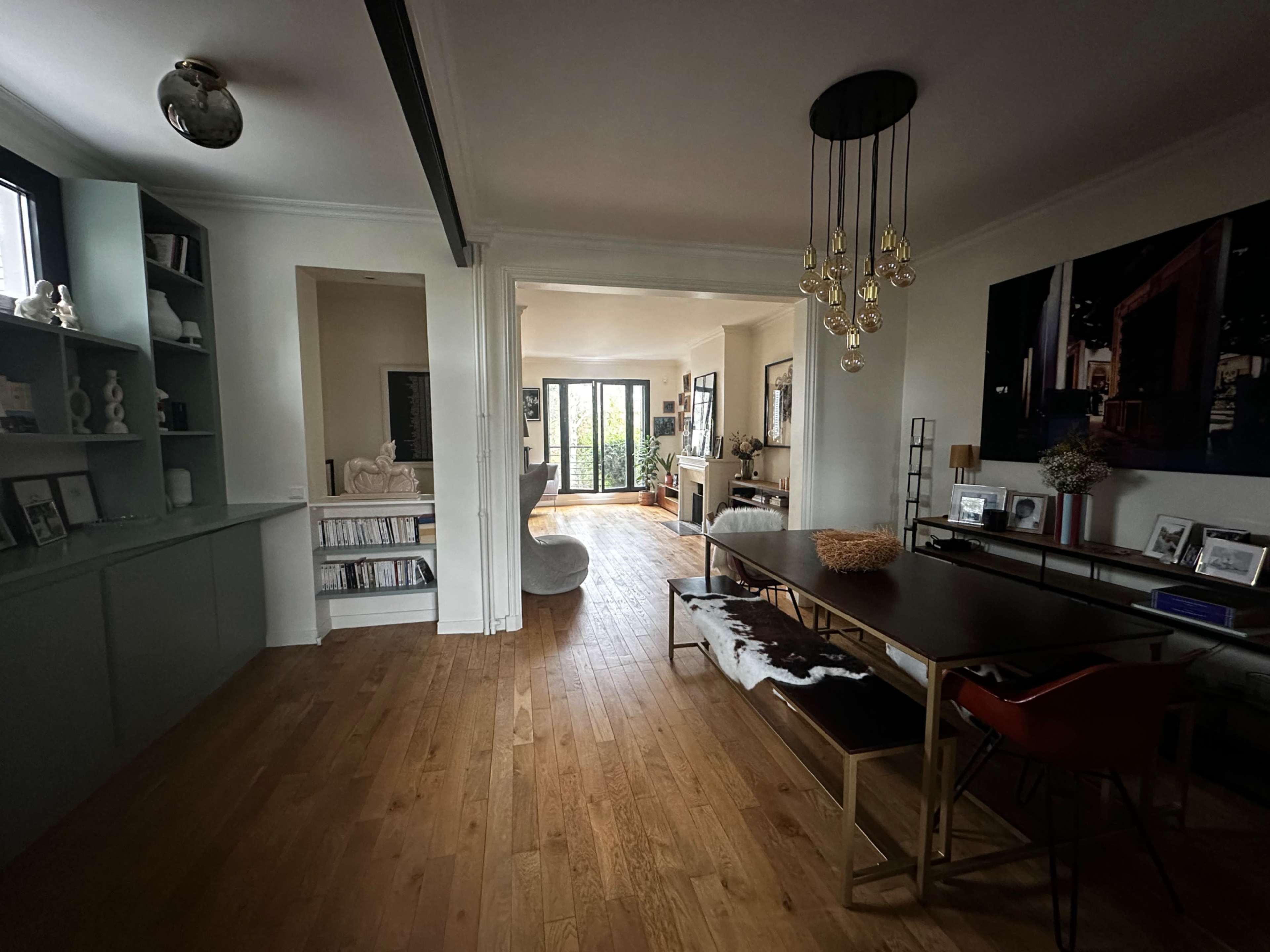 The image shows a spacious living area connected to a dining space, featuring hardwood floors, a large window, and modern decor elements.