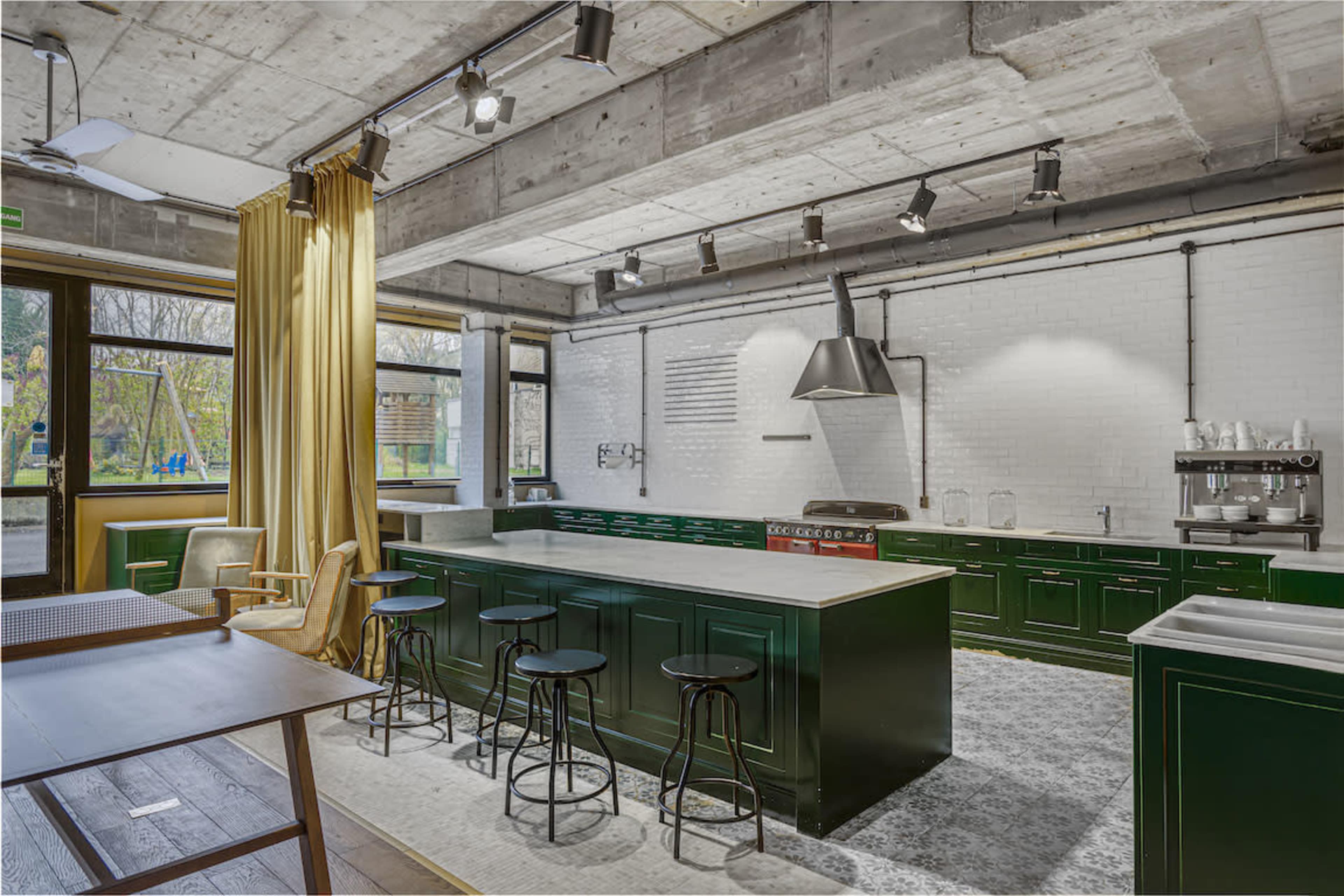 A modern kitchen with green cabinetry, a large island with barstools, and large windows providing natural light.