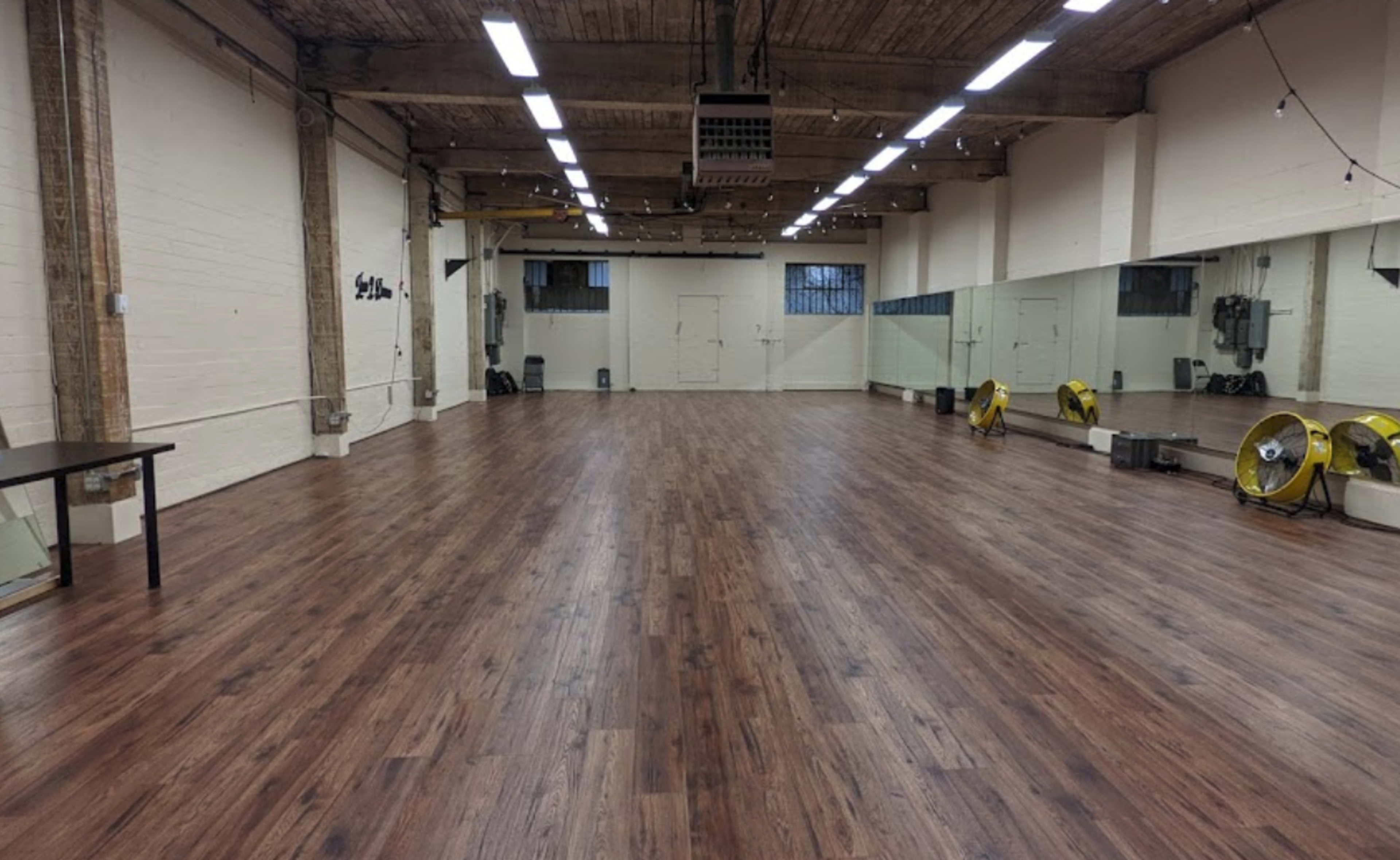 A spacious, empty room with wooden flooring and large mirrors on one wall.