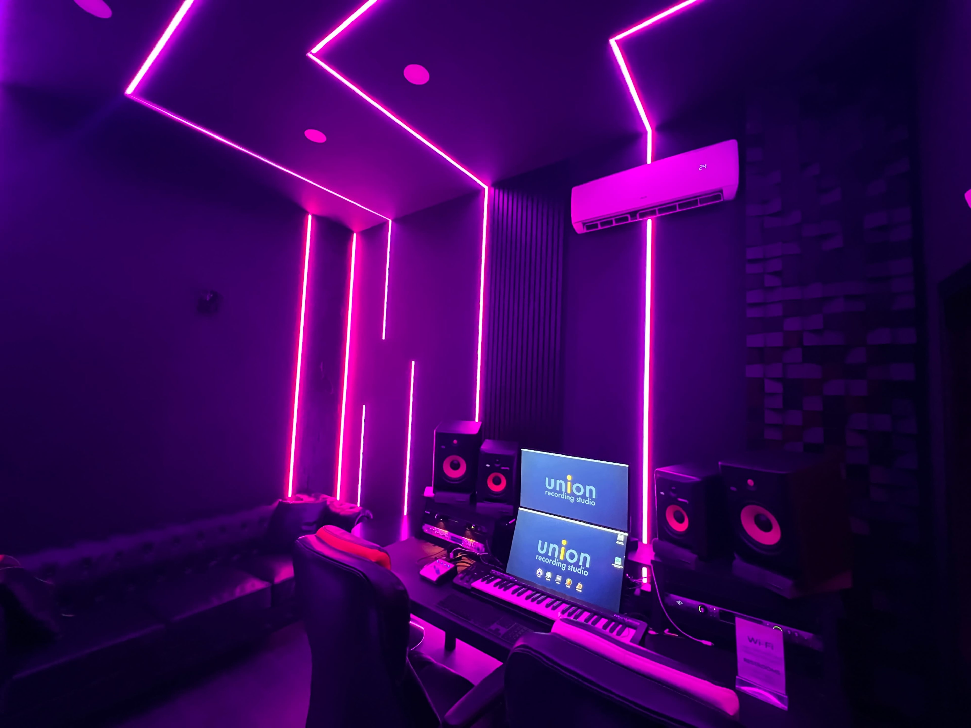 A music studio featuring a dark interior with purple LED lighting, a piano keyboard, and audio equipment.
