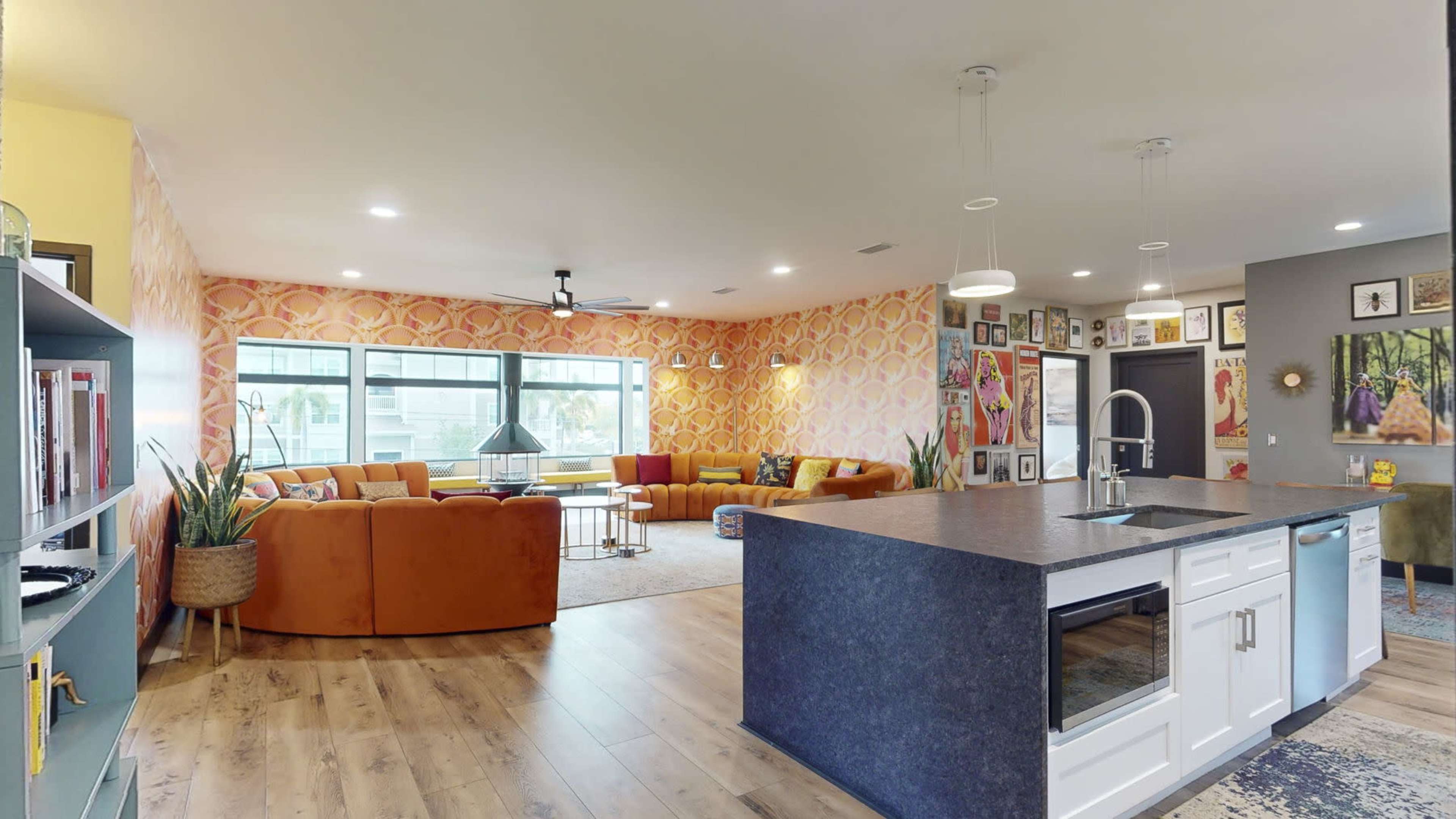 A modern living room with orange sectional sofas, a kitchen island with a dark countertop, and a wall adorned with framed artworks.