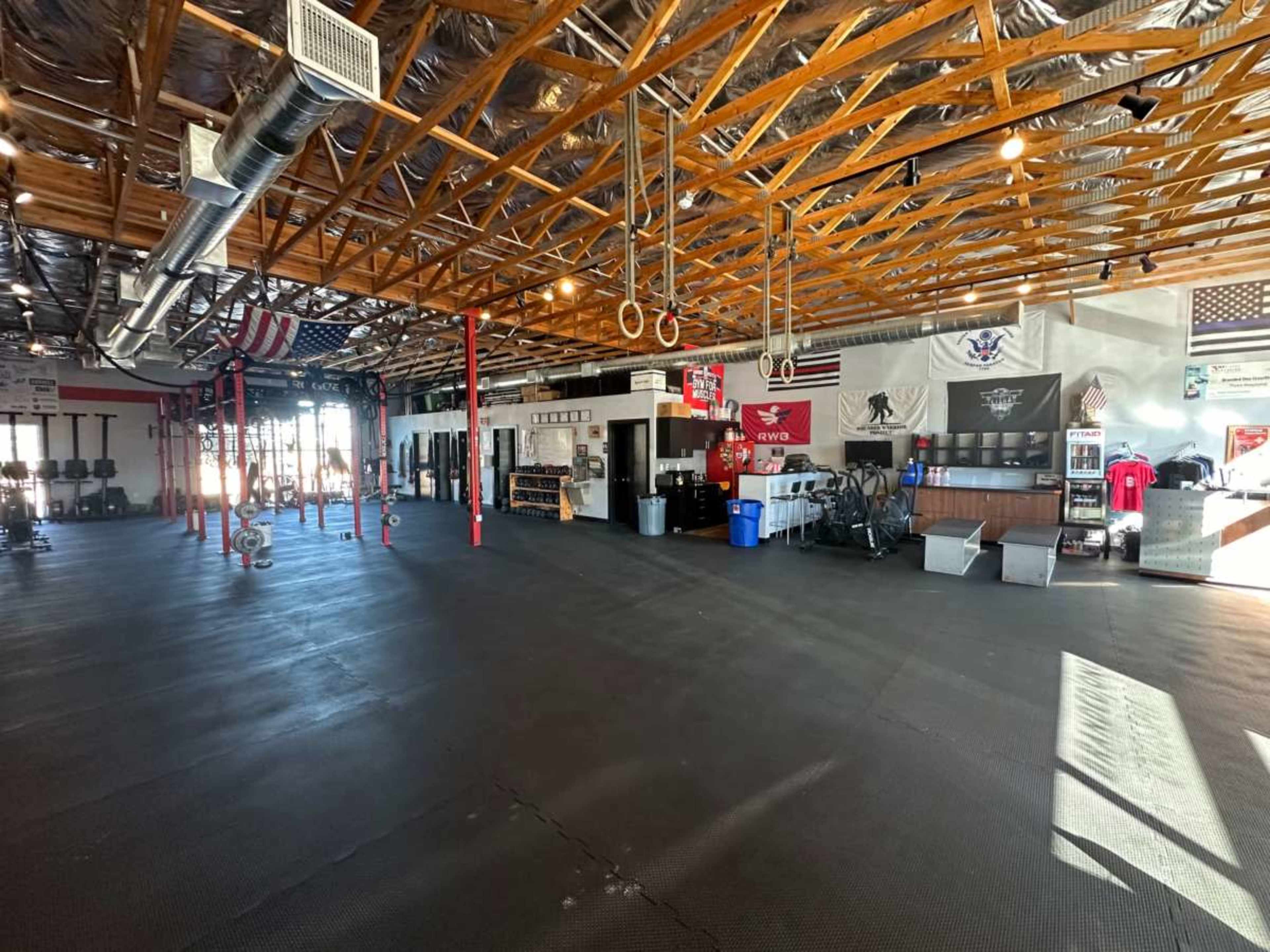 An indoor gym with a spacious floor, exposed wooden beams, various workout equipment, and several flags displayed on the walls.