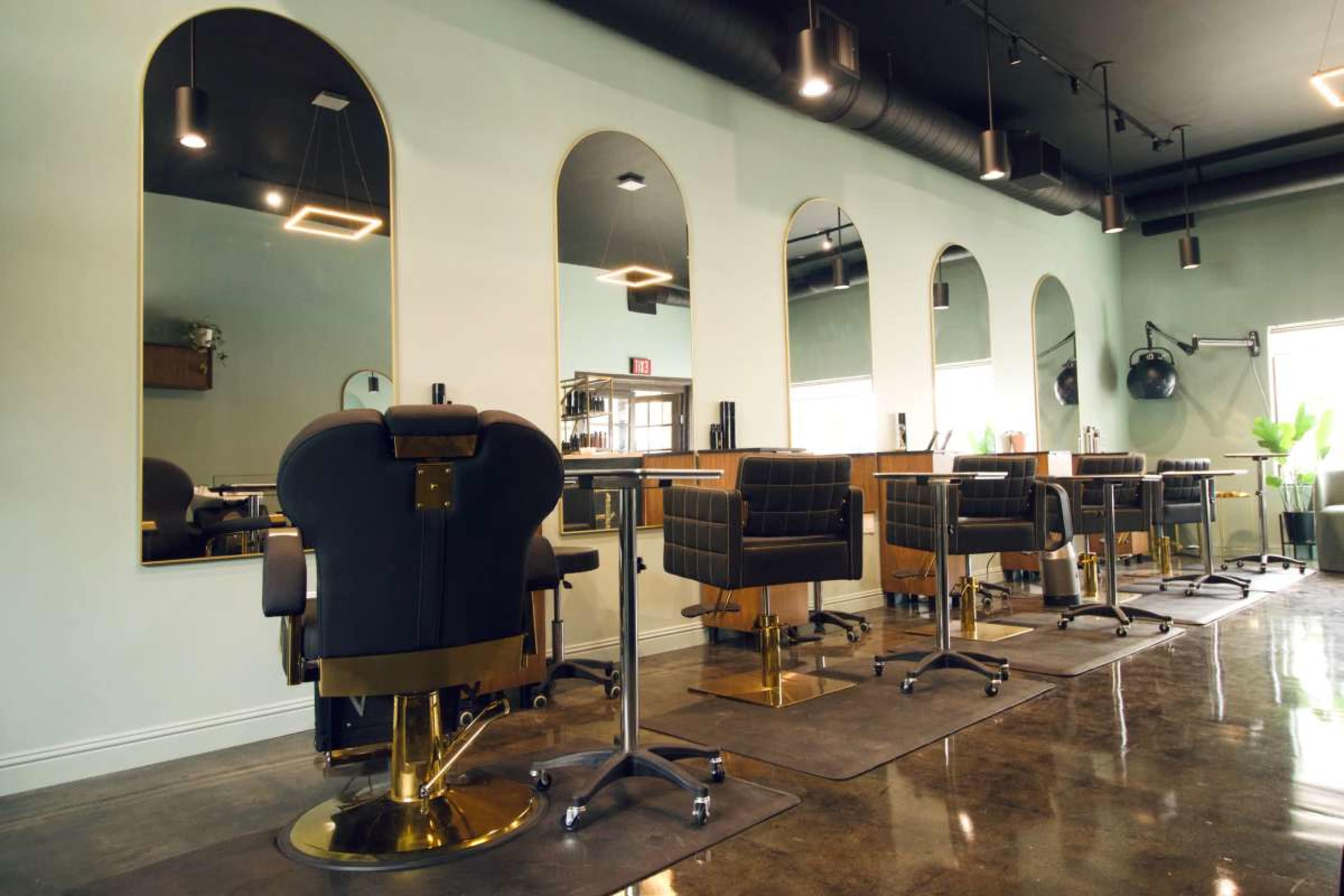 The image shows a modern hair salon with multiple styling stations featuring black chairs and large mirrors against a light-colored wall.
