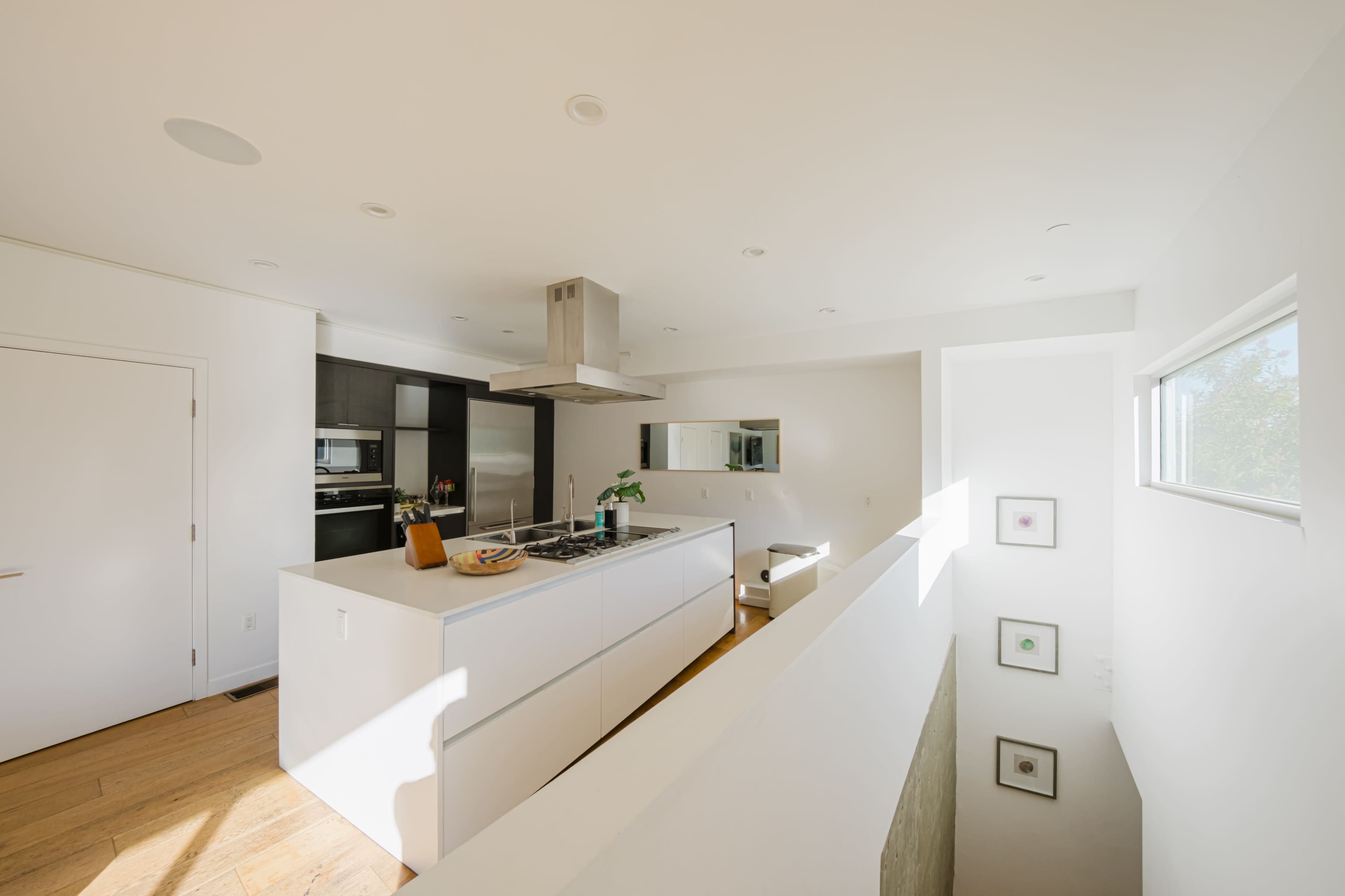 The image shows a modern kitchen with a central island, sleek cabinetry, and large windows providing natural light.