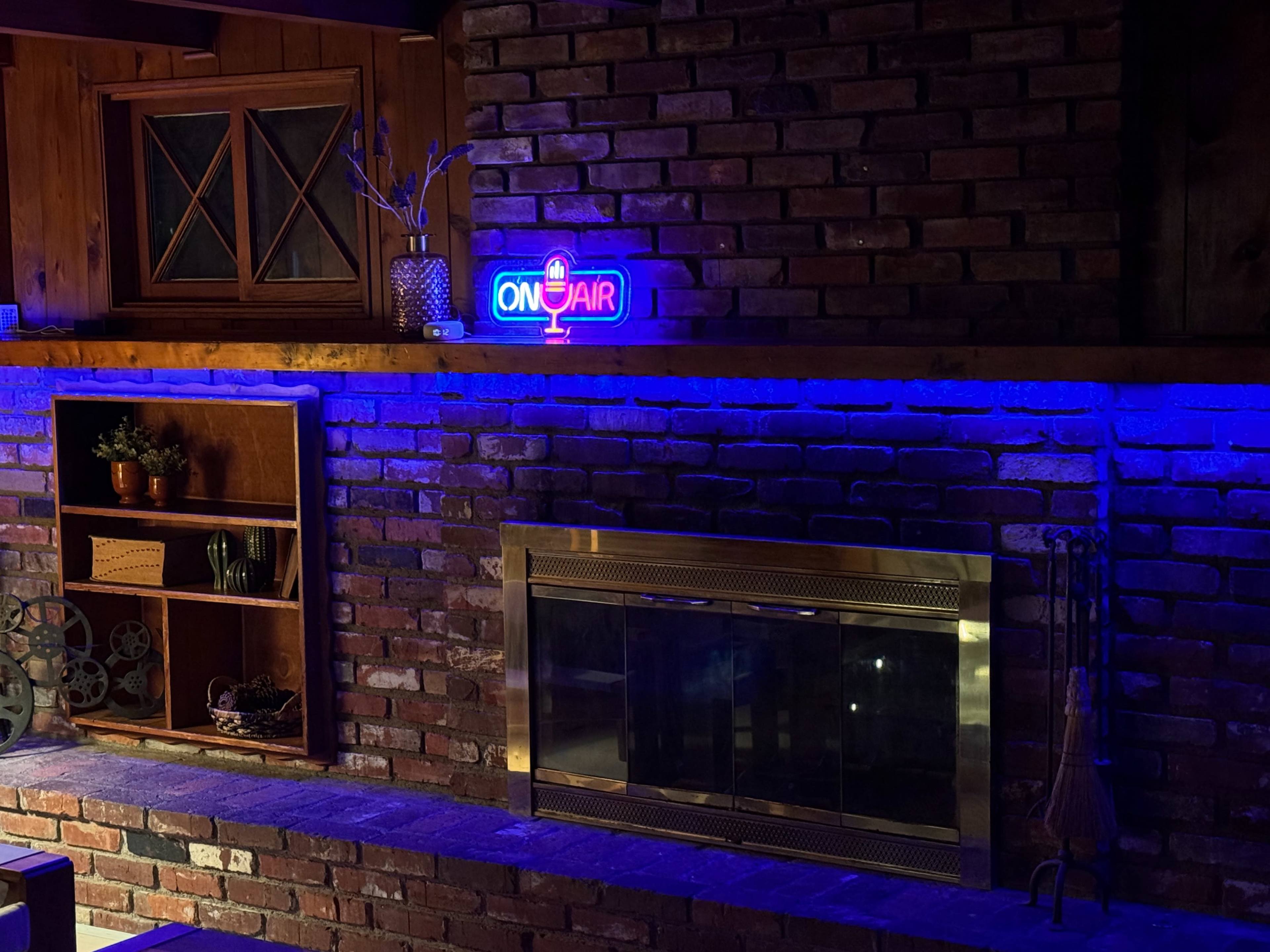 The image shows a brick wall with a fireplace beneath a neon "ON AIR" sign and blue ambient lighting.