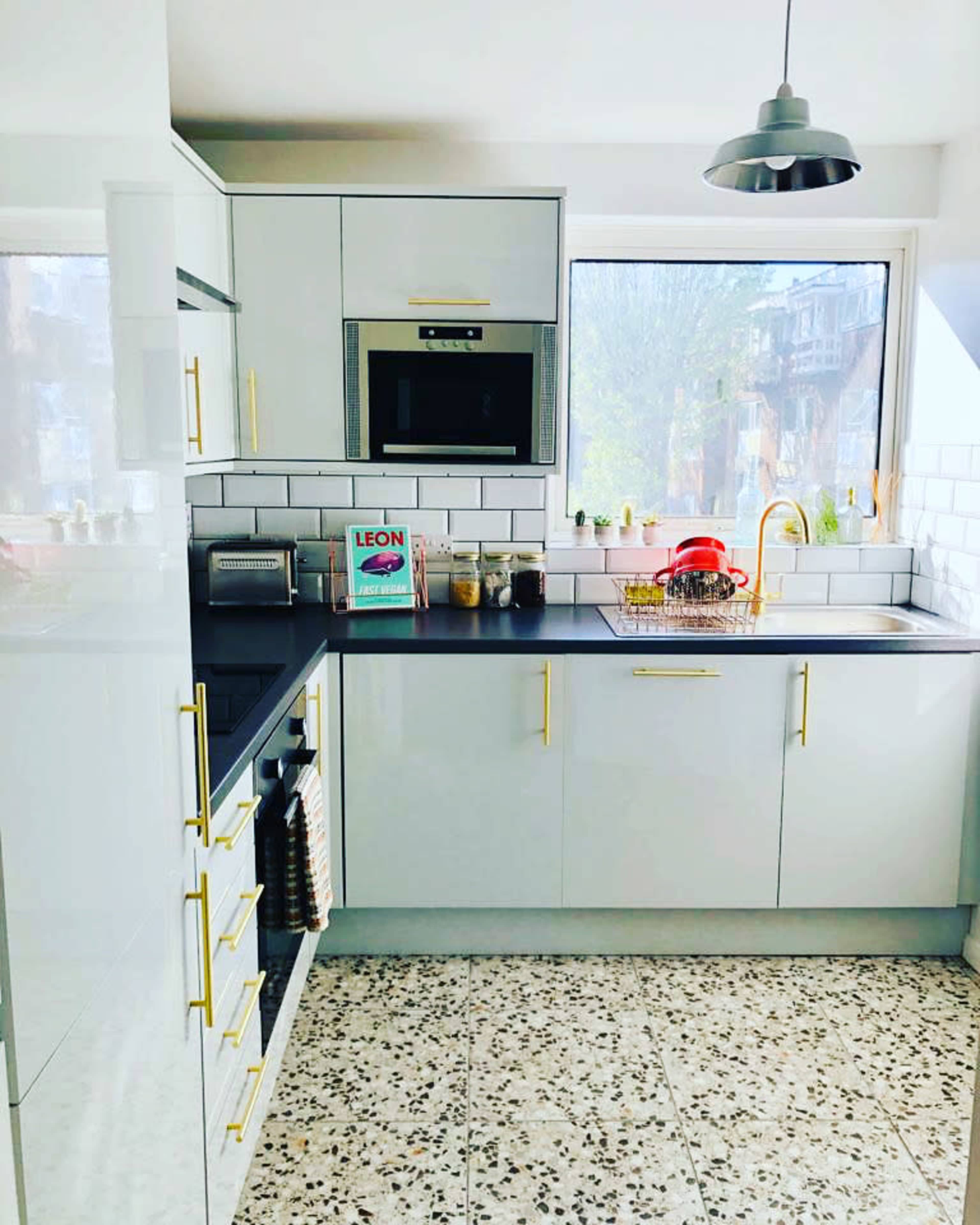 A modern kitchen features white cabinetry, a microwave, and a sink with a golden faucet, set against a backdrop of patterned tile flooring.