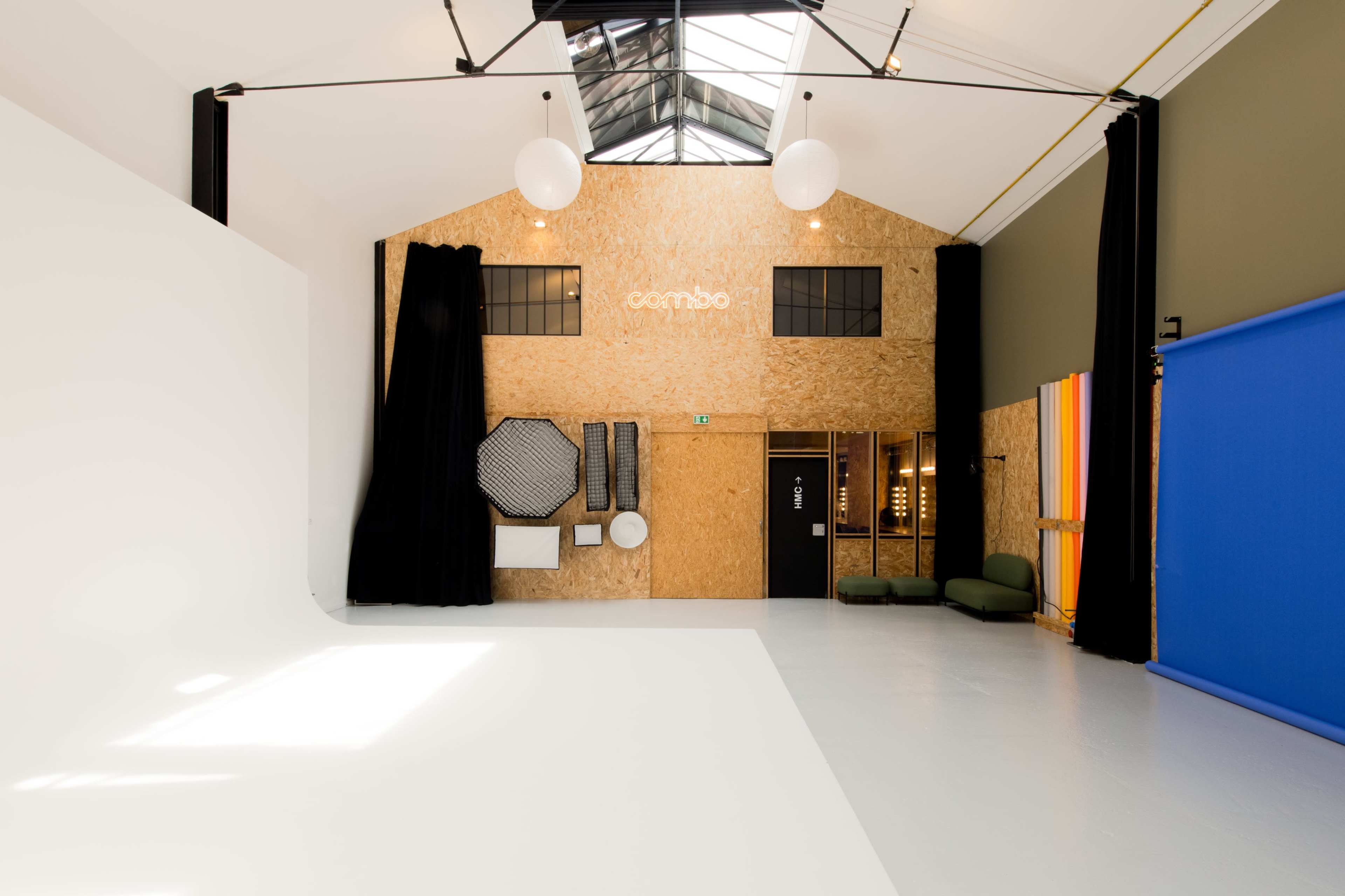 A spacious studio with an open layout featuring wooden walls, a high ceiling with skylights, and a large white floor area, alongside various photography equipment and backdrop options.