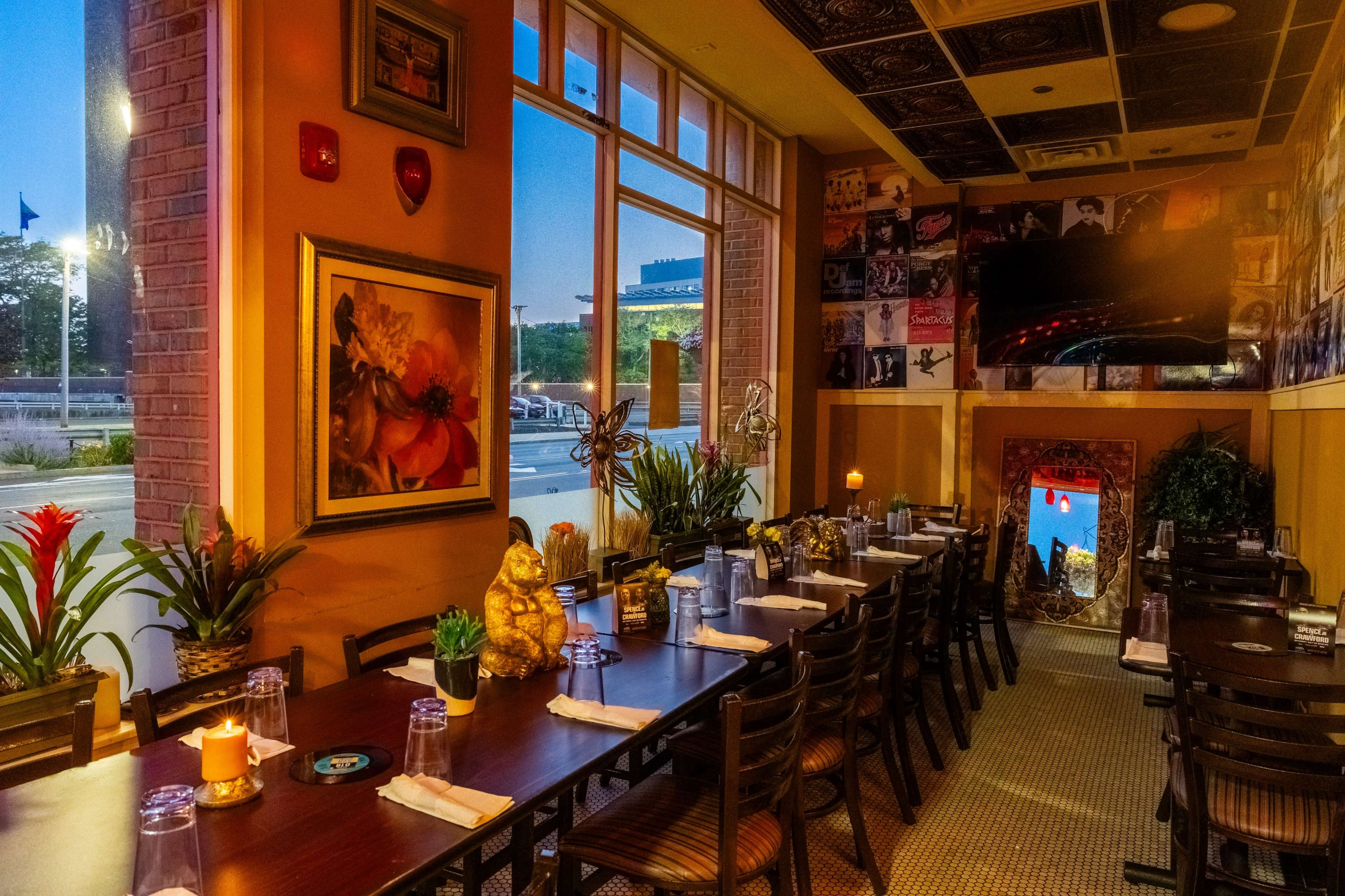 A restaurant interior featuring tables set for dining, adorned with plants, candles, and decorative artwork on the walls.
