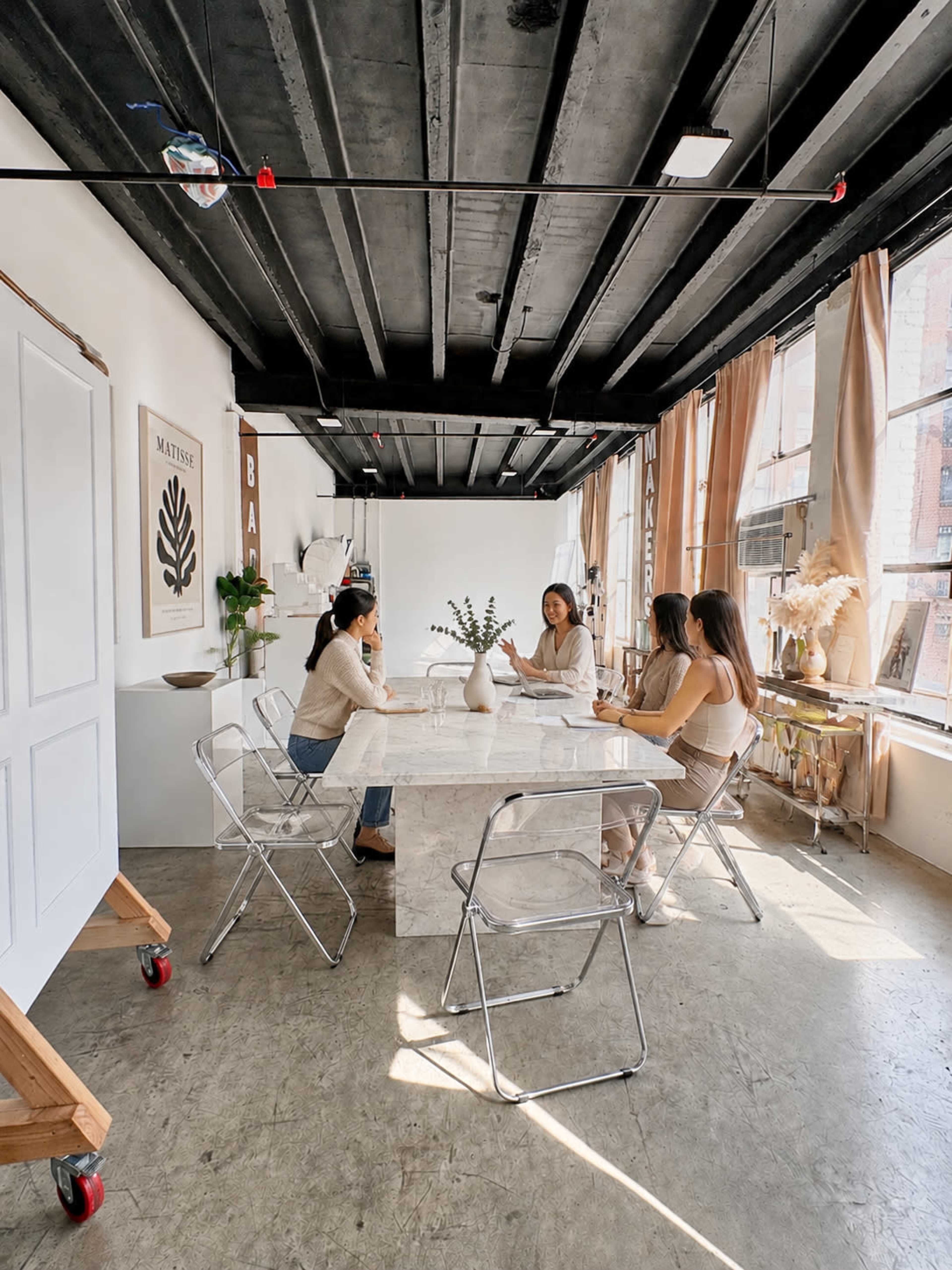 A group of four individuals sits around a large, clear table in a modern room with natural light and minimalist decor.