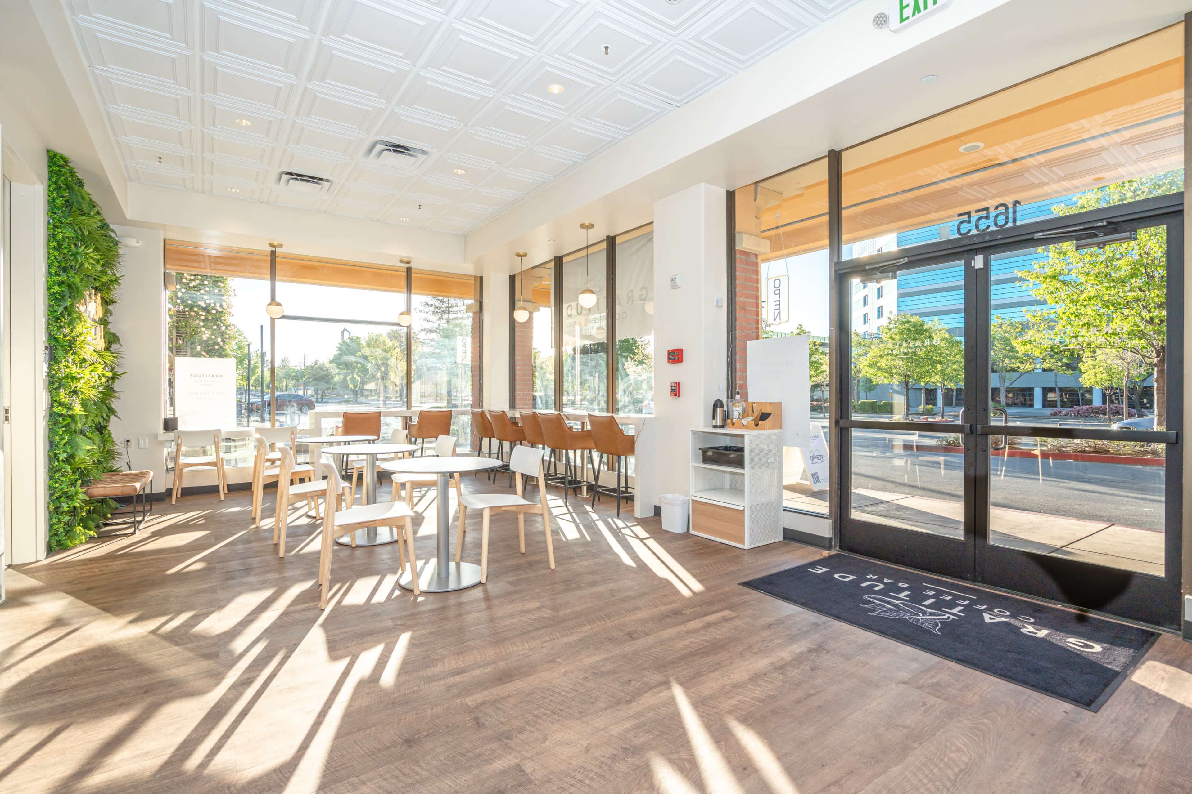 A bright, modern cafe interior with wooden flooring, large windows, and a mix of tables and chairs.