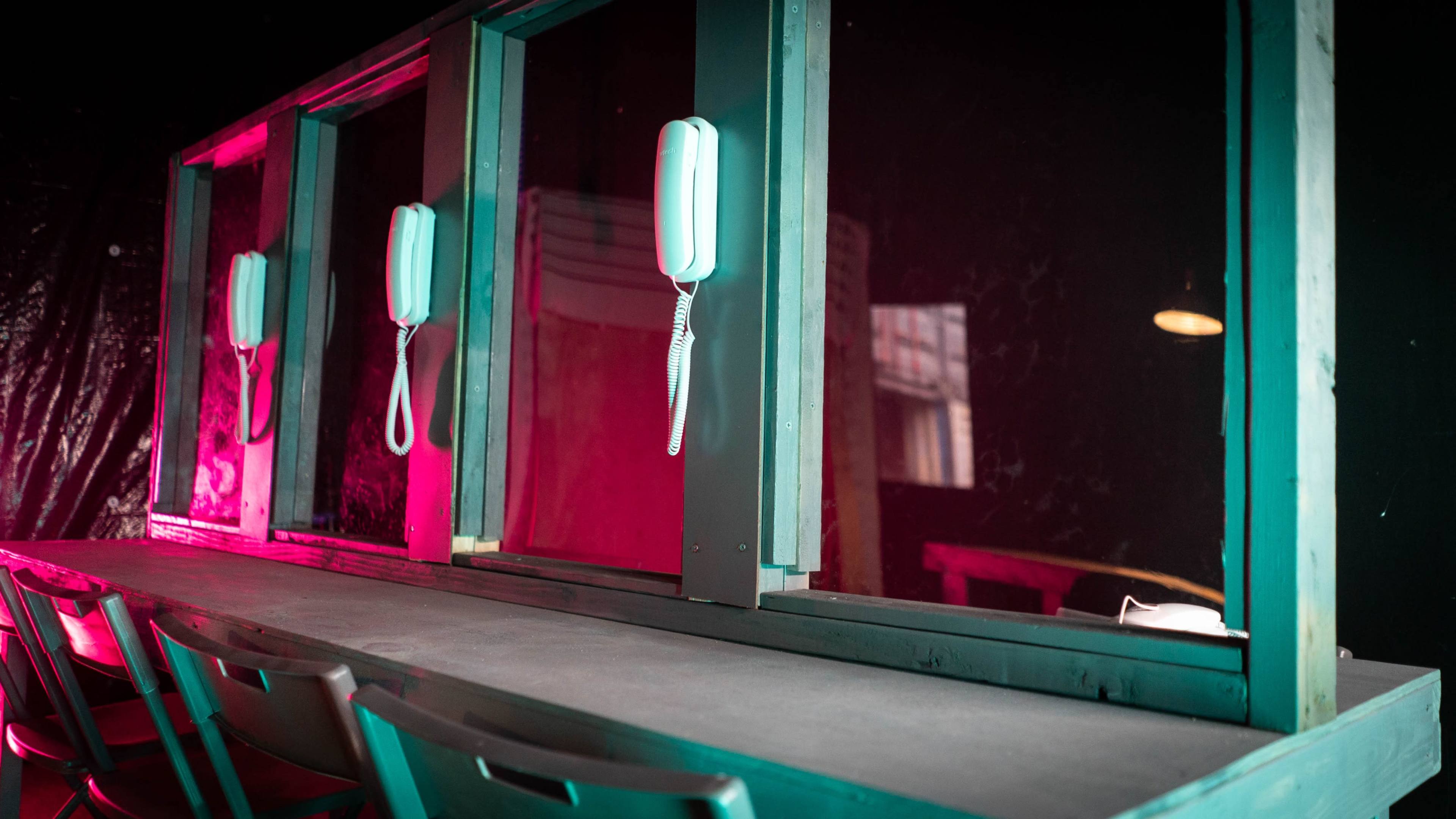 A dimly lit counter with three retro-style telephones mounted on a partition with colorful lighting.