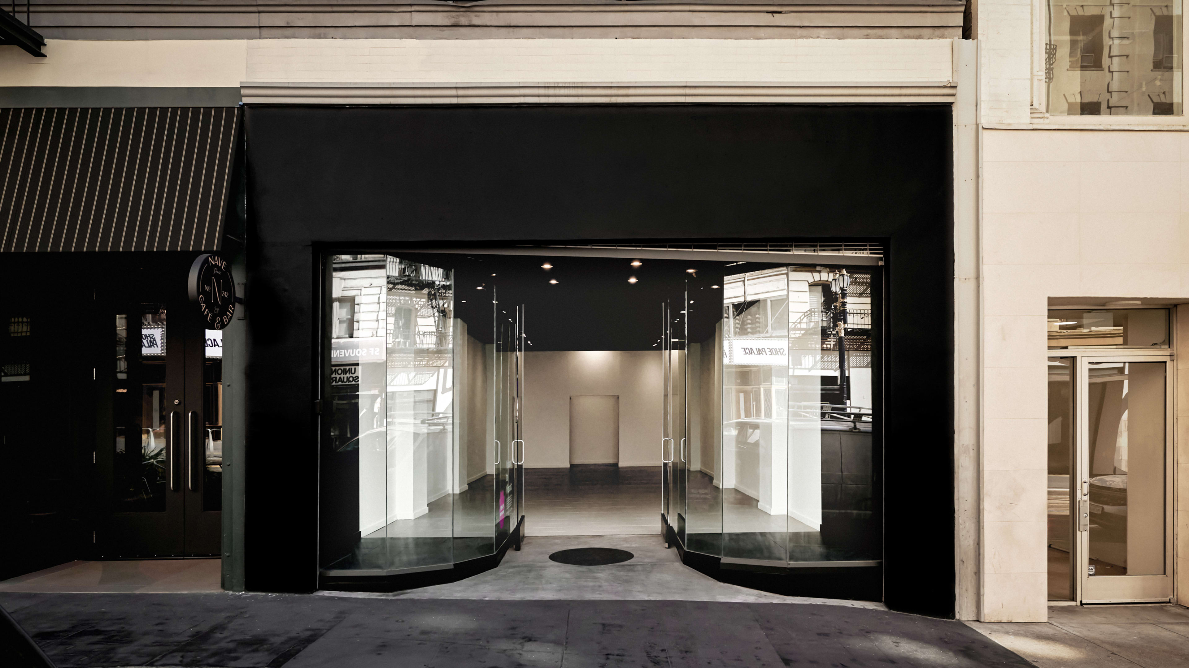 The image shows a modern storefront with large glass windows and an open entryway on a city street.
