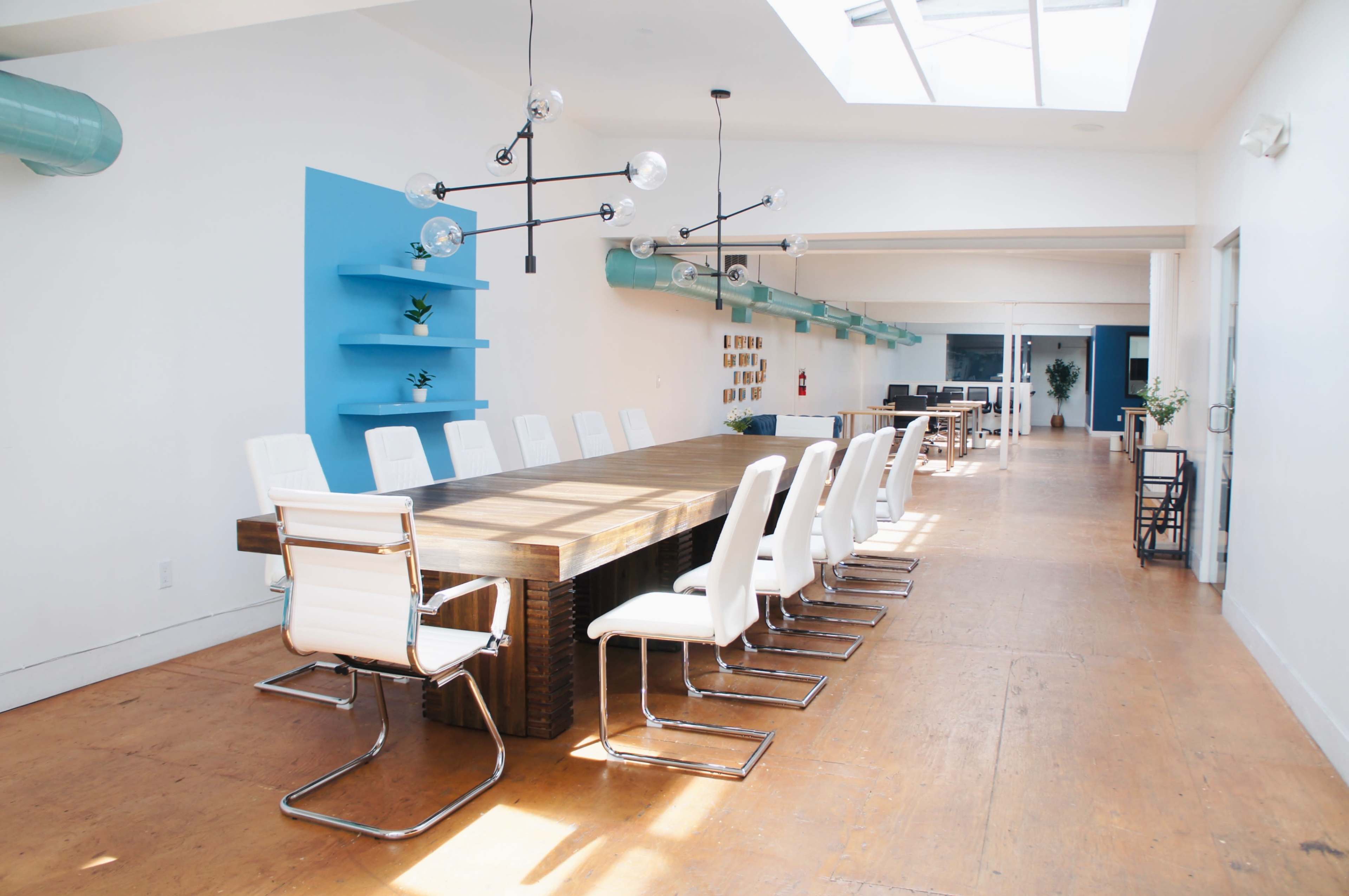 The image shows a modern conference room with a long wooden table surrounded by white chairs, blue accent walls, and large windows allowing natural light.