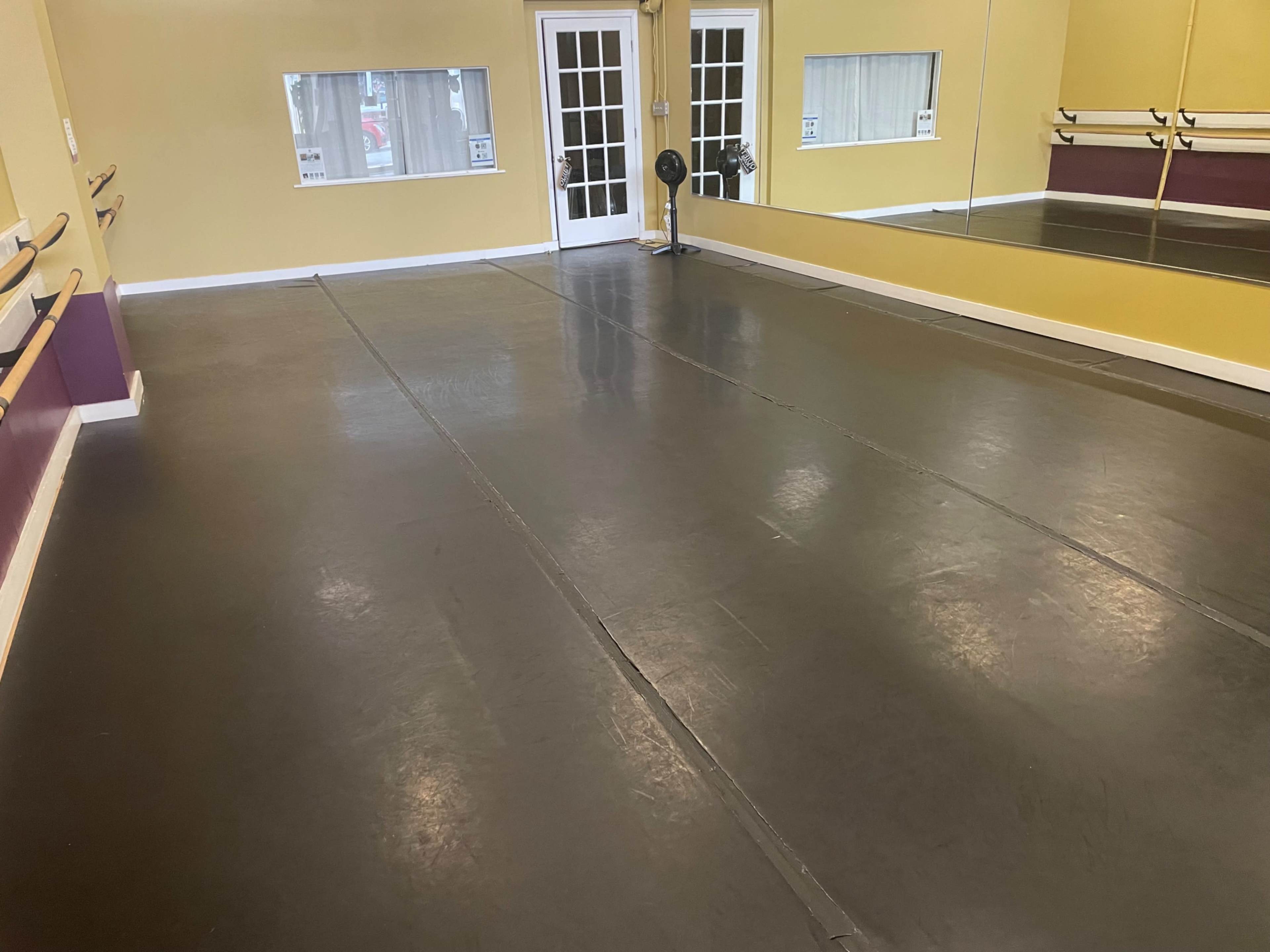 The image shows an empty dance studio with a smooth, dark floor, mirrored walls, and barres along one side.