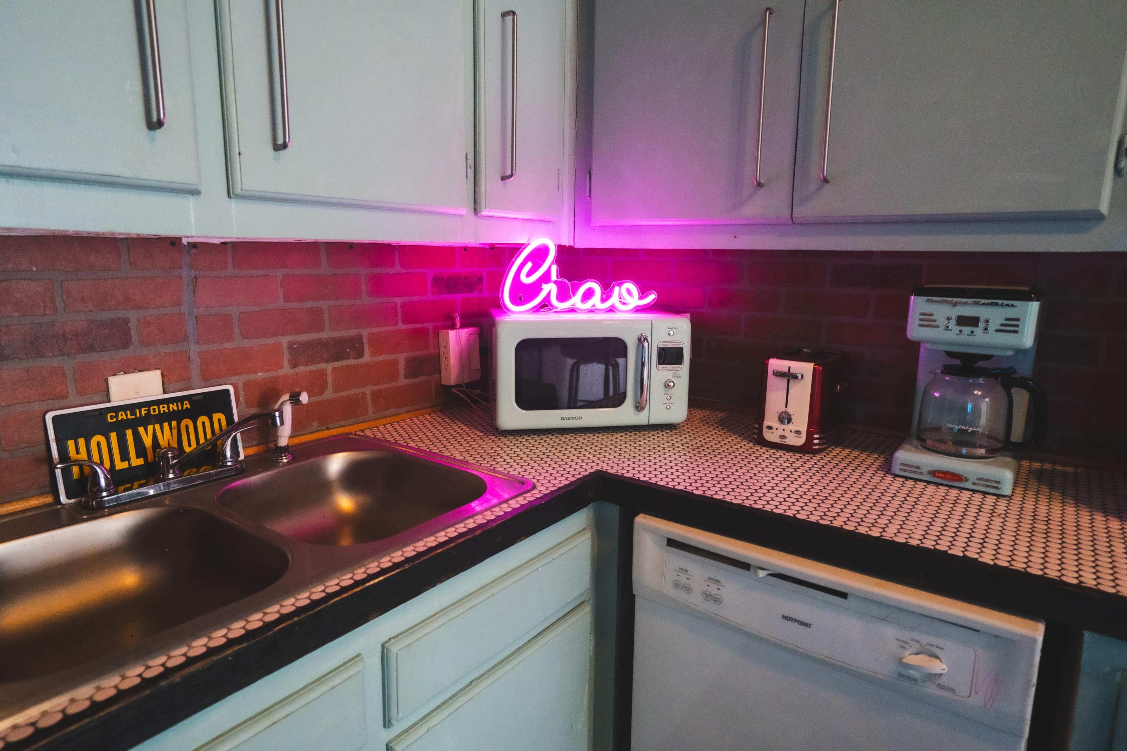 The kitchen features a microwave, a coffee maker, and a neon sign reading "Crav" against a backdrop of brick and light blue cabinets.