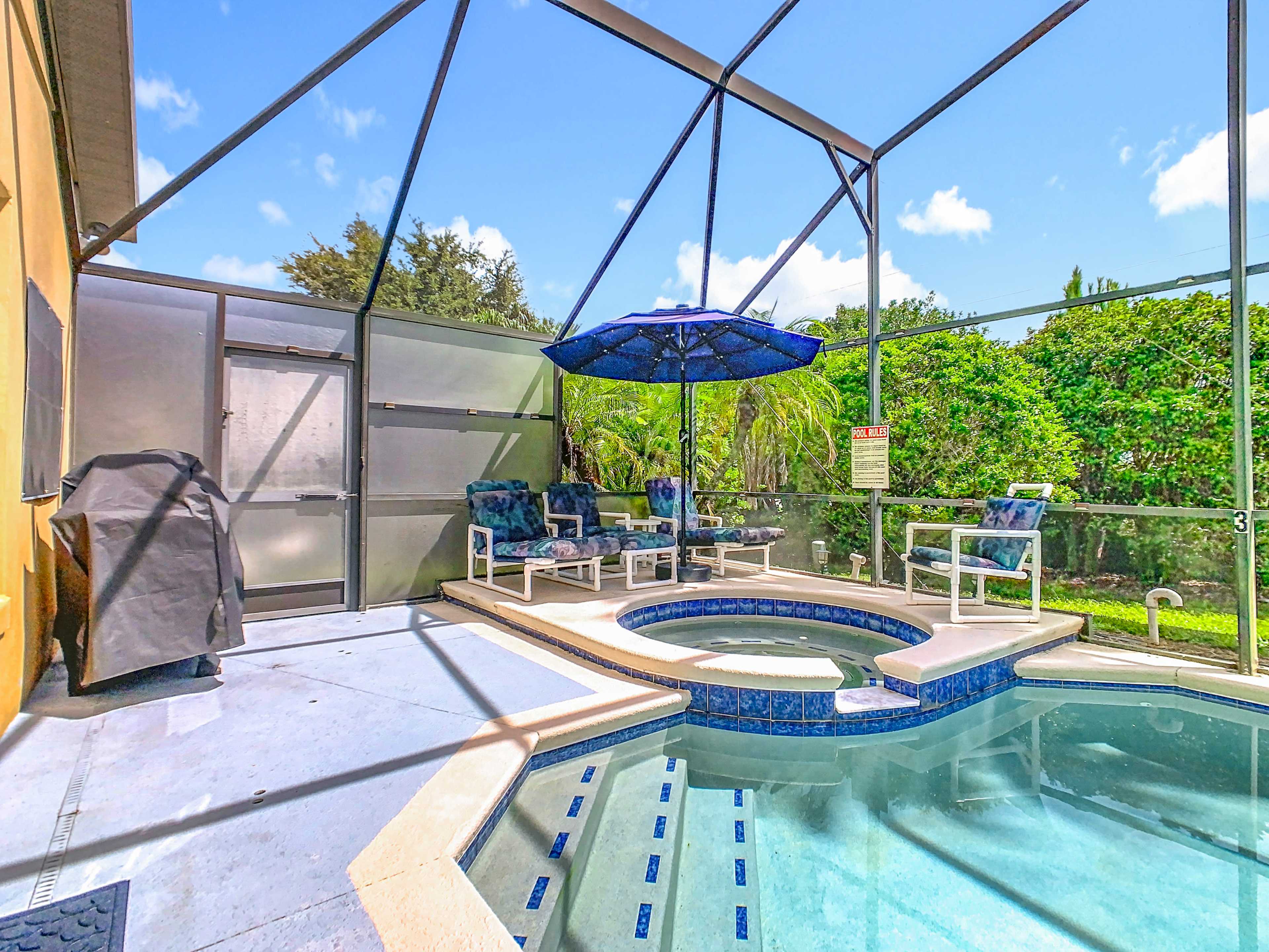 The image shows a screened-in pool area with a hot tub, outdoor seating, and a large umbrella.