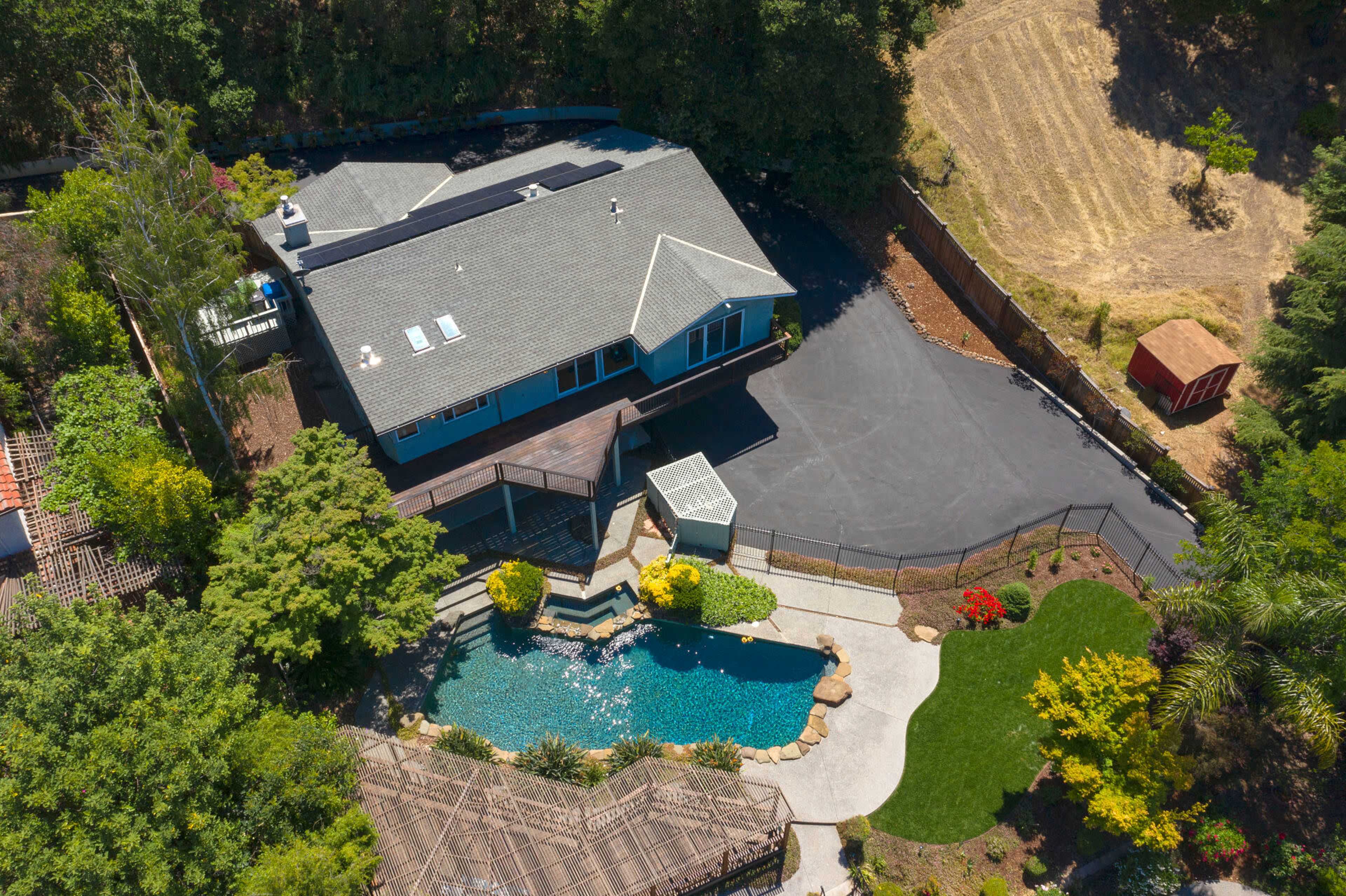 An aerial view of a house with a swimming pool surrounded by landscaping in a rural setting.