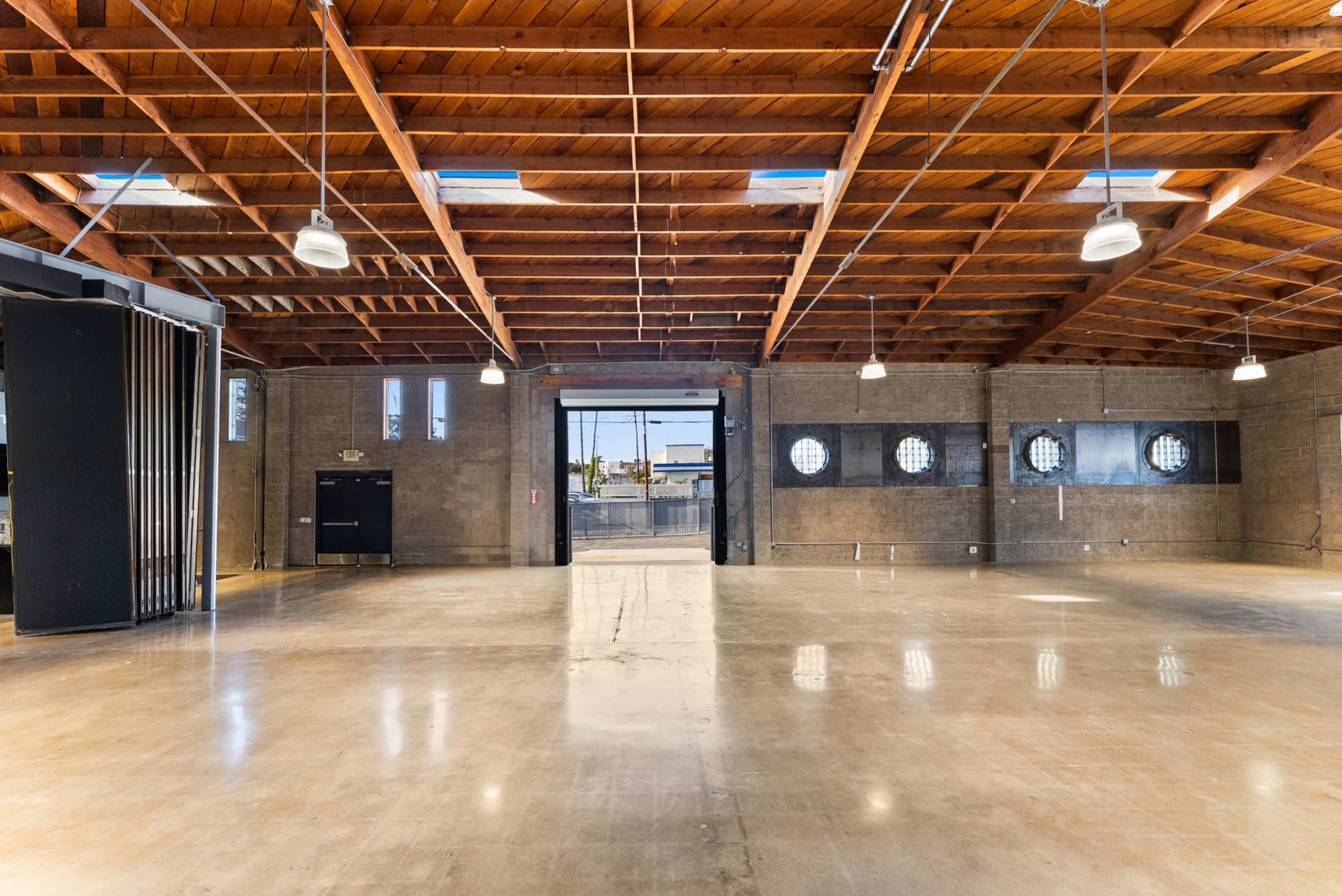 The image shows an expansive, empty commercial space with high wooden beams and large circular windows.