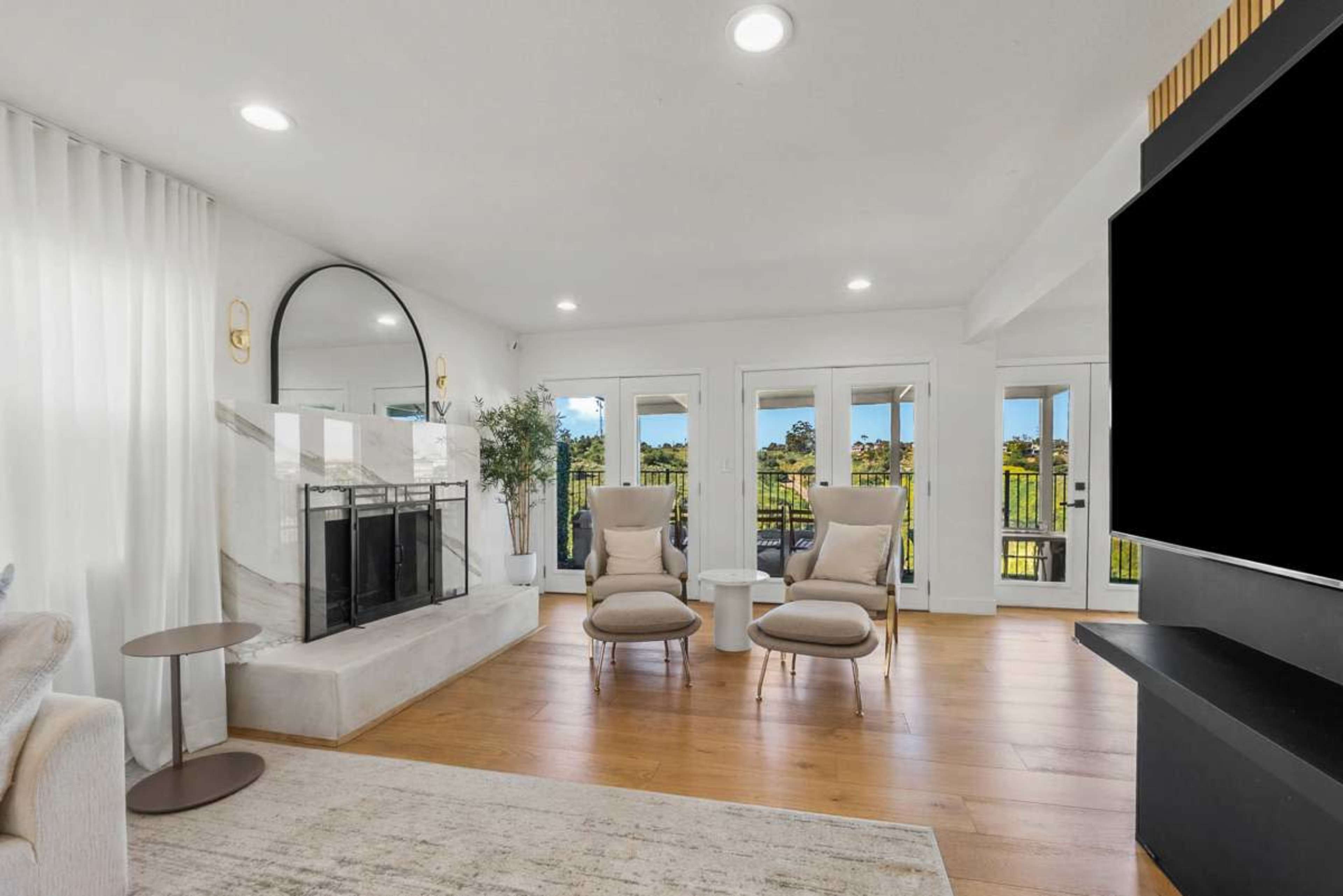 The image features a modern living room with two armchairs facing a stylish fireplace and large windows that open to a view of greenery.