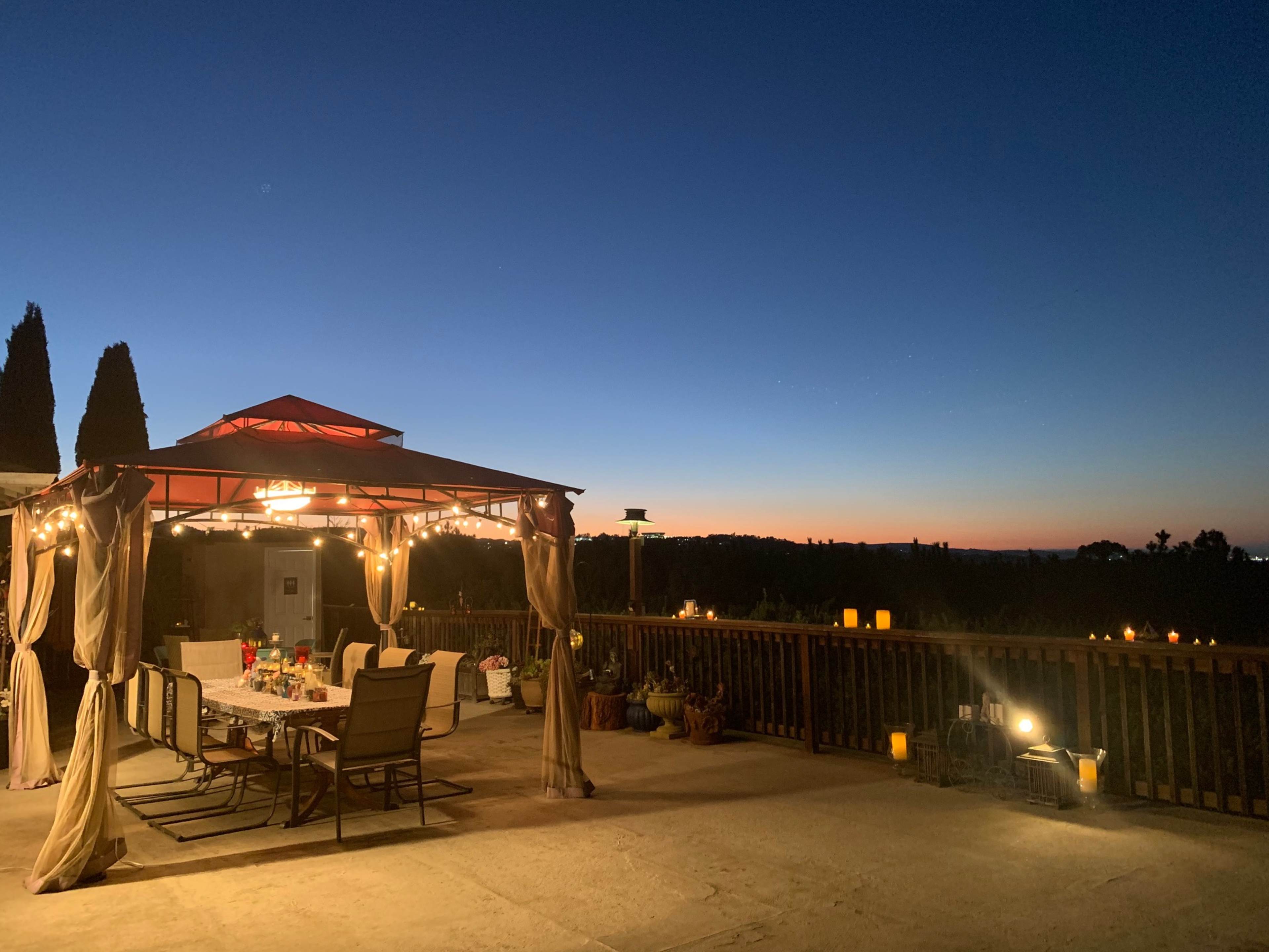 A covered outdoor dining area is illuminated by string lights, set against a twilight sky.