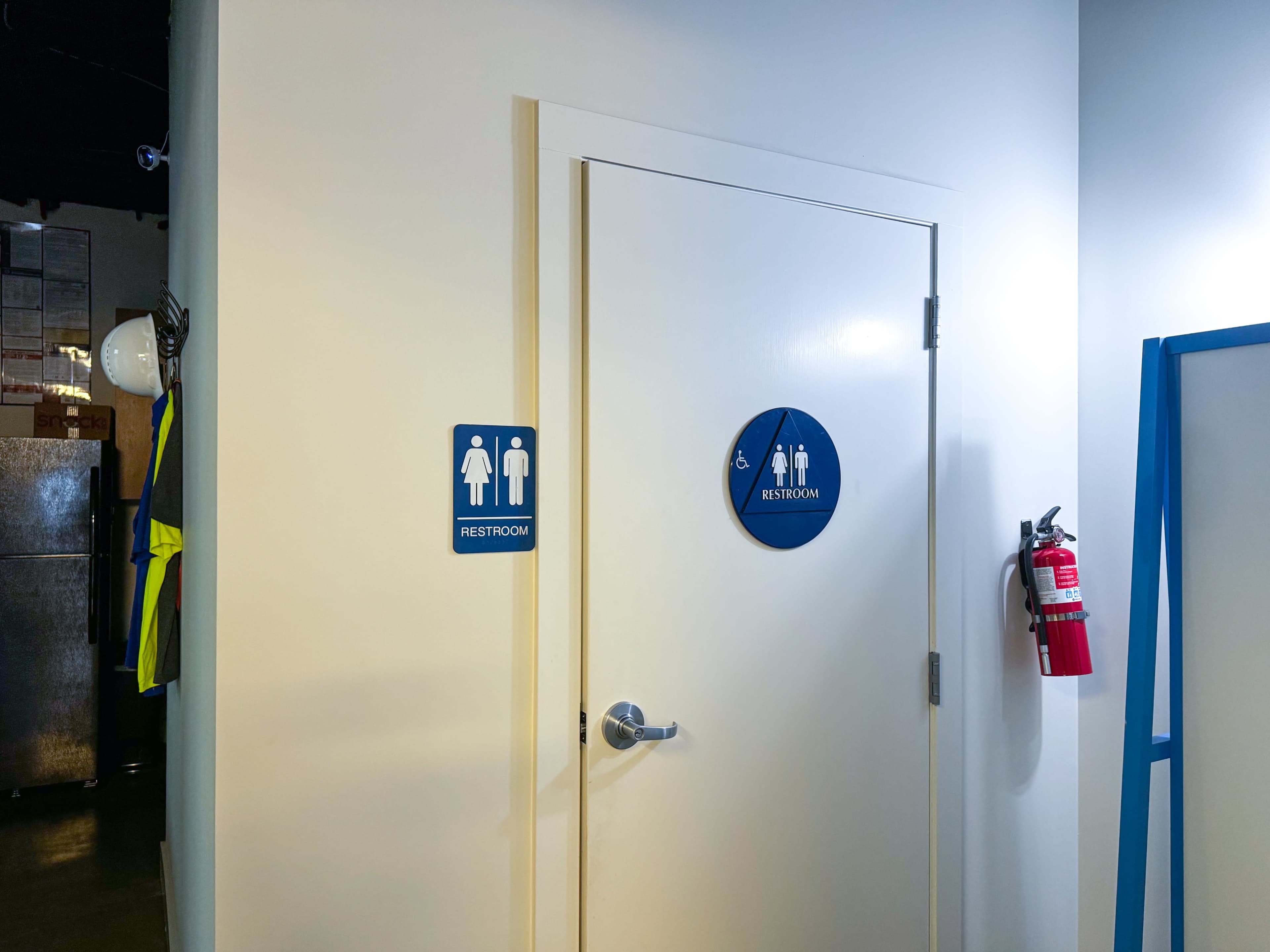 A restroom door with signs indicating the presence of a men's and women's restroom, and a fire extinguisher mounted on the wall nearby.