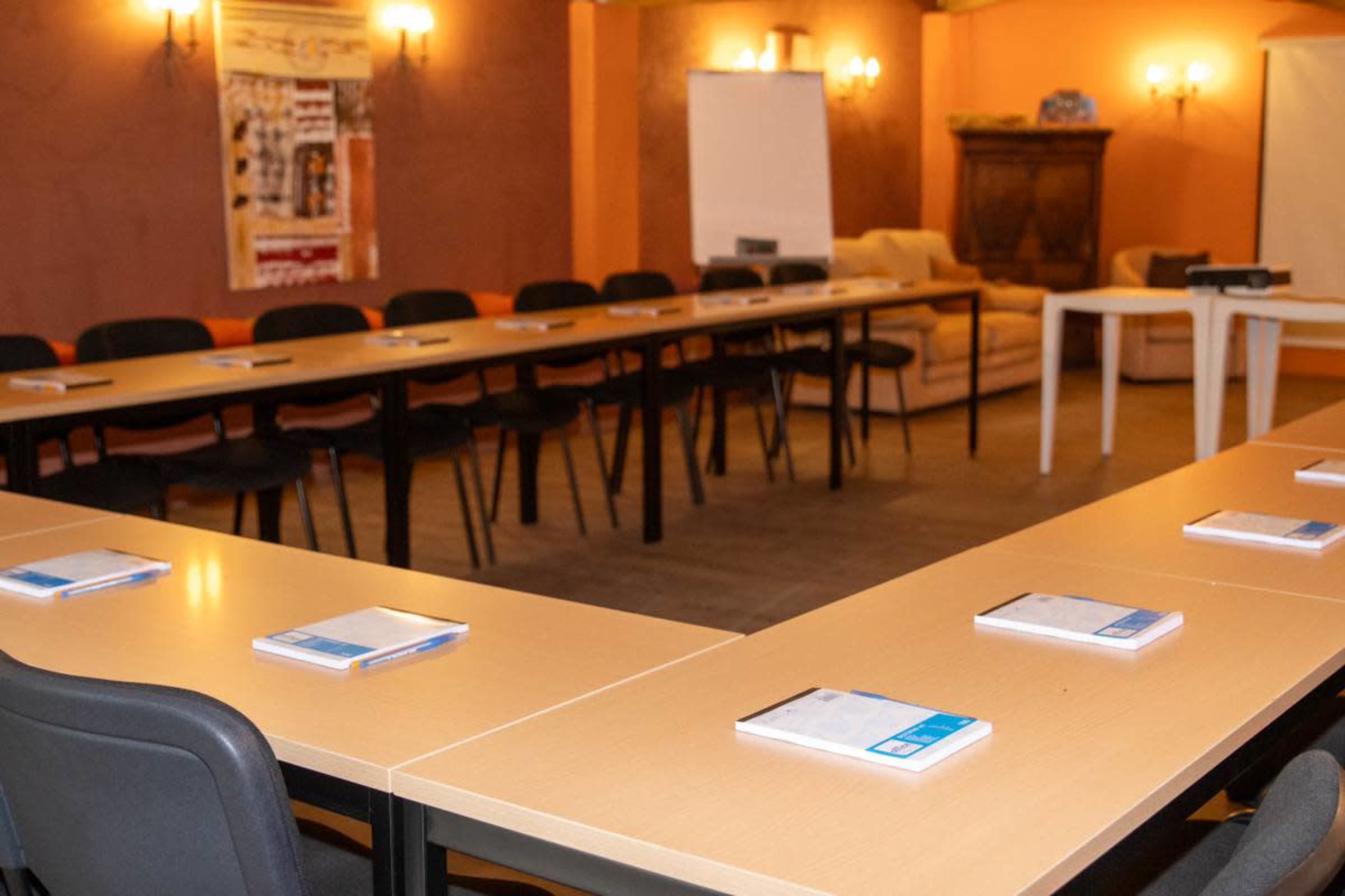 The image shows a meeting room with several tables arranged in a U-shape, each covered with notebooks and a projector nearby.