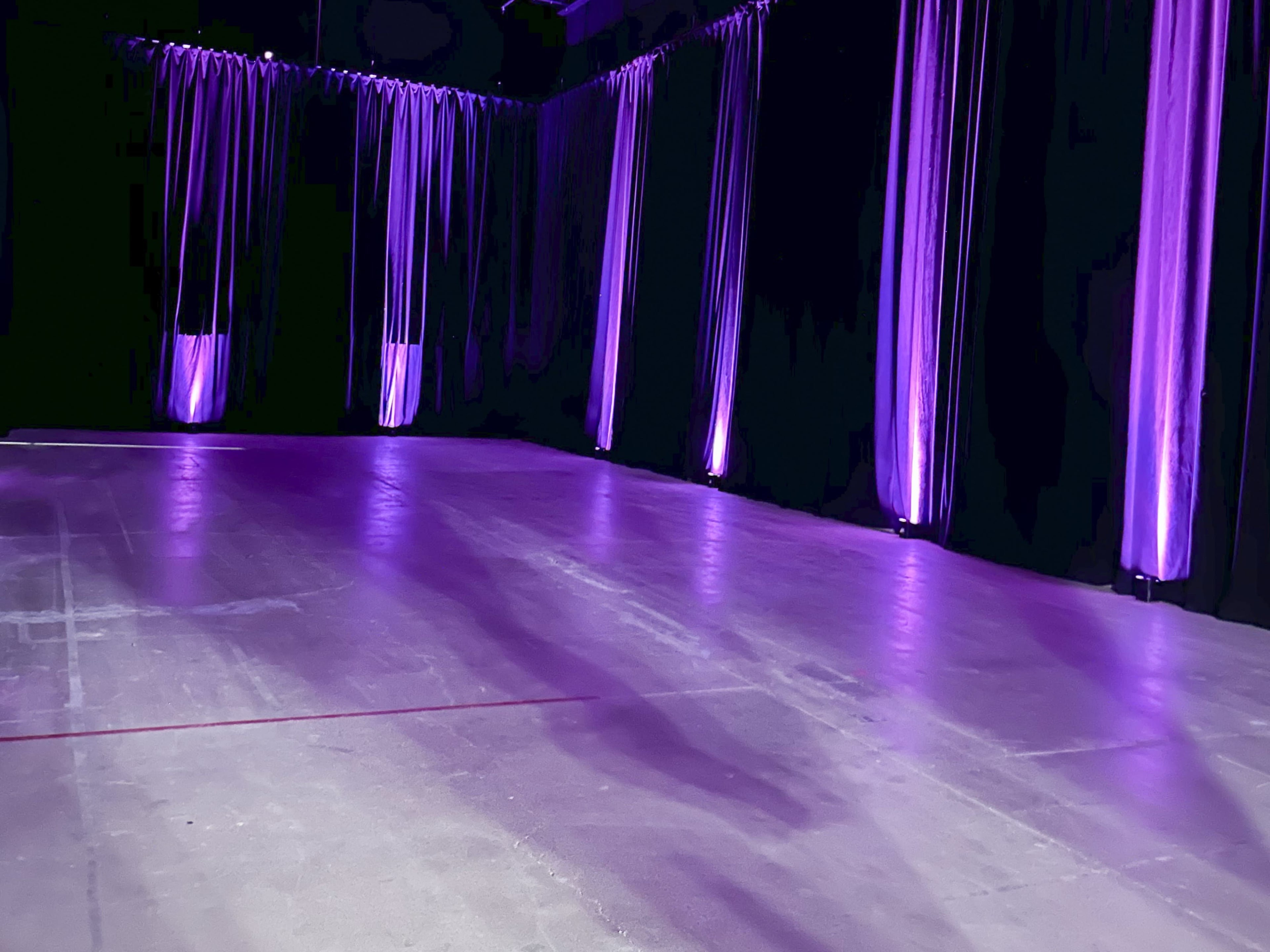 A dimly lit room with purple lighting and long fabric drapes along the walls.