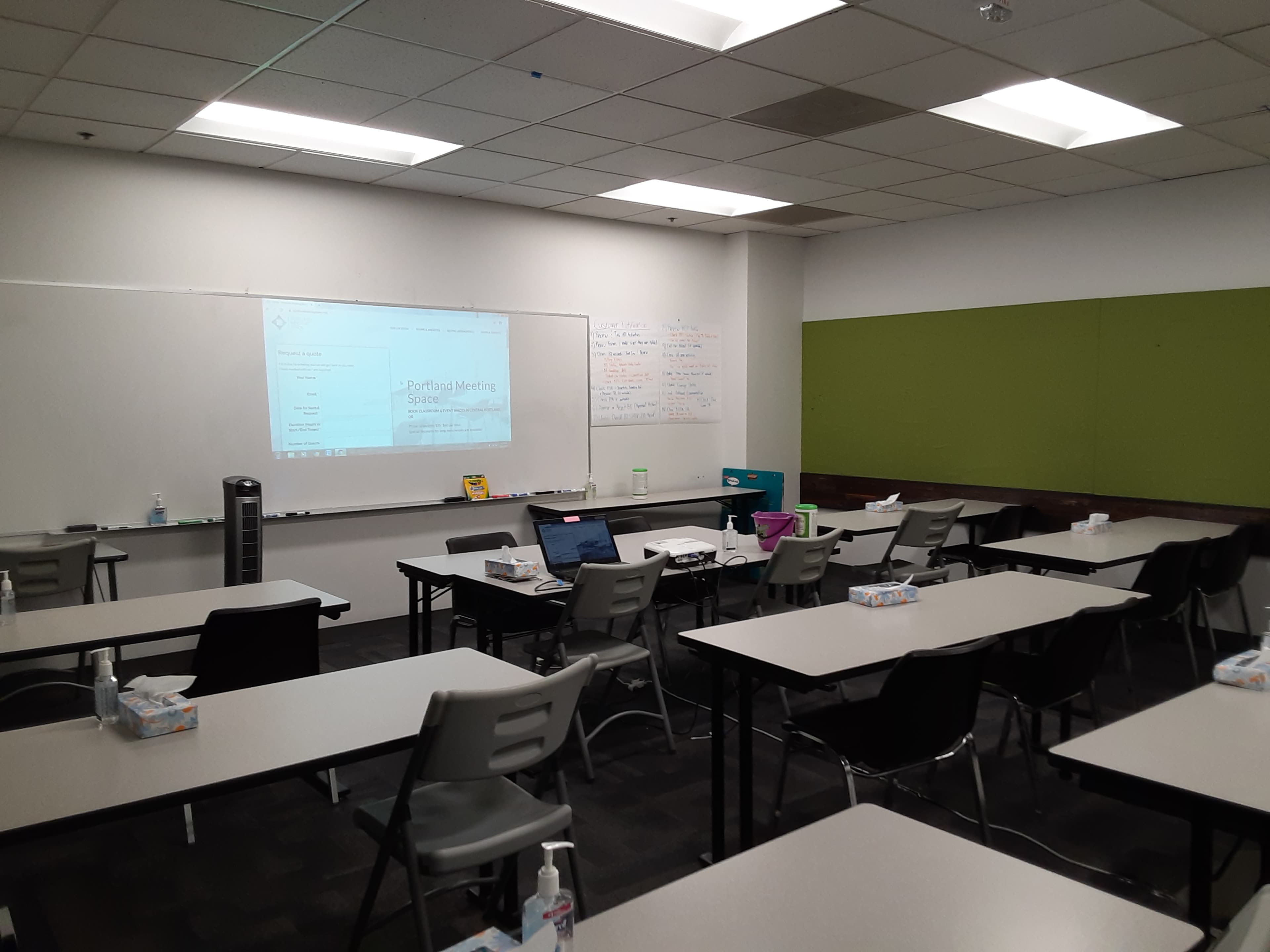 A classroom features rows of tables and chairs, with a projector displaying a presentation on a screen at the front.