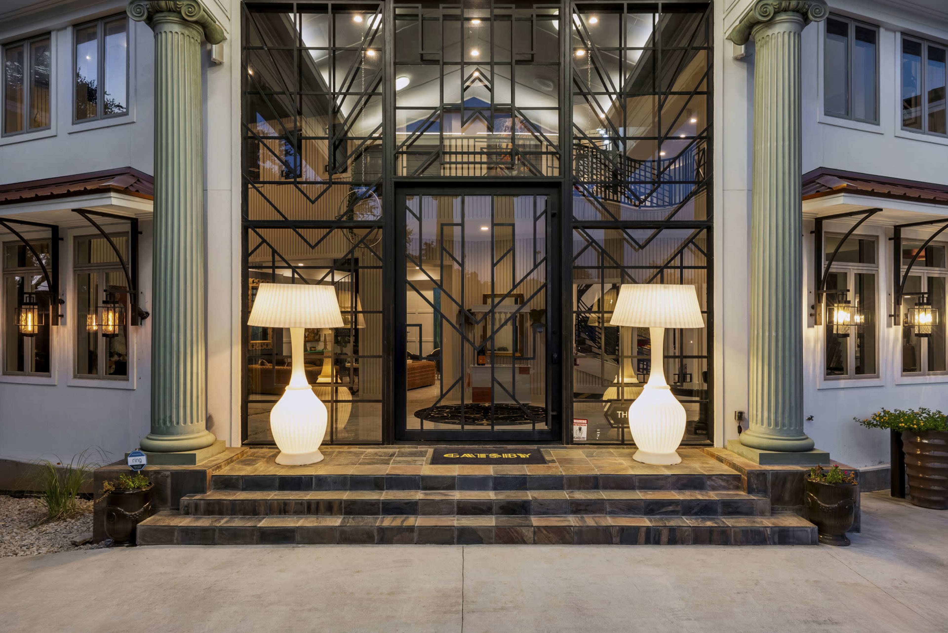 A modern entrance with large glass doors, flanked by two illuminated lamps and flanked by classical columns.