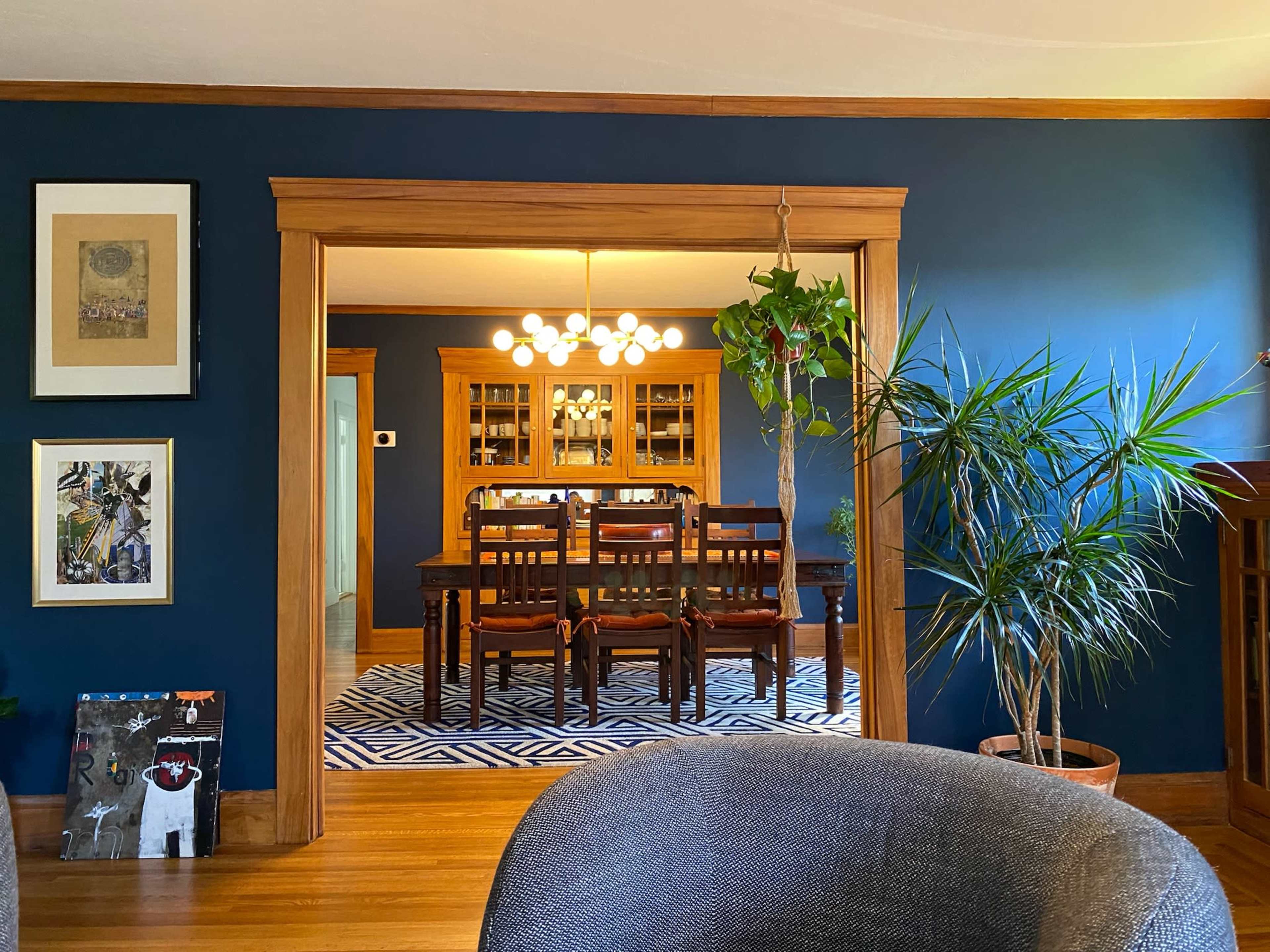The image shows a dining area with a dark blue wall, wooden furniture, and a patterned rug, visible through an arched doorway.