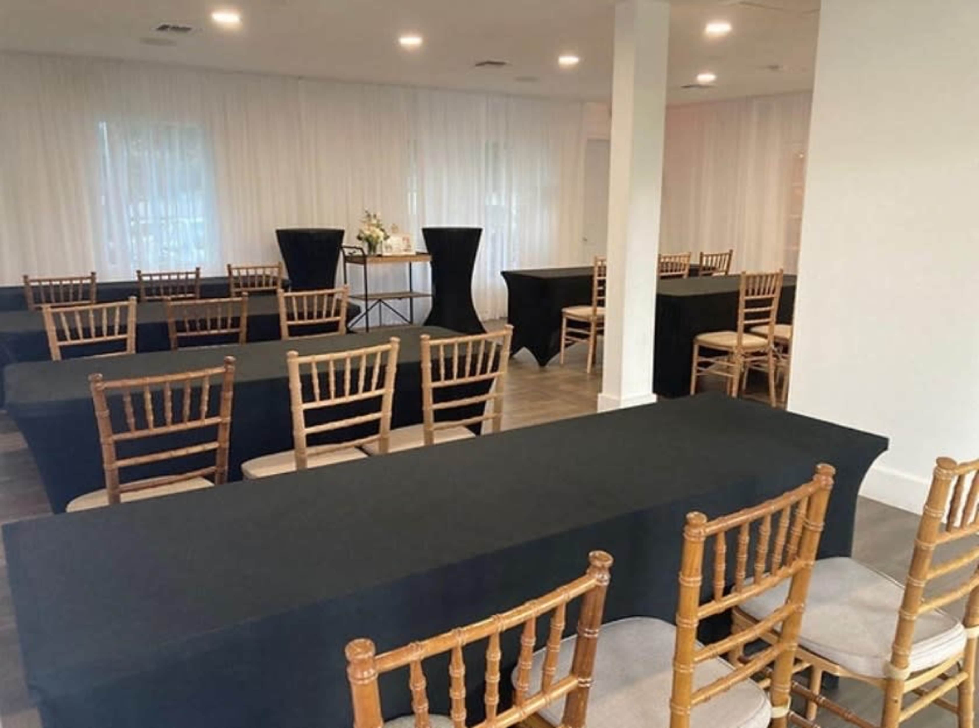 A banquet-style room with multiple rows of black tables and golden wooden chairs arranged for an event.