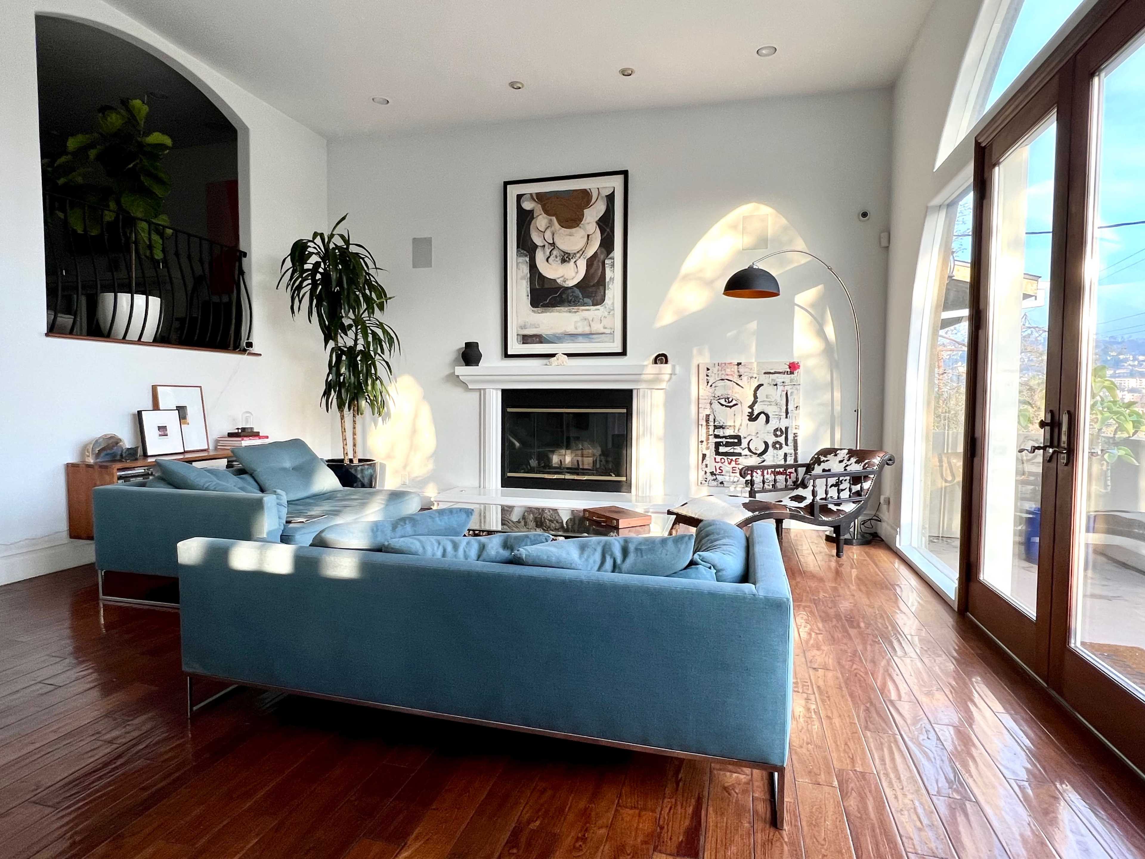 The interior features a modern living room with a light blue sofa arrangement, a fireplace, and large doors leading to a view of the outdoors.