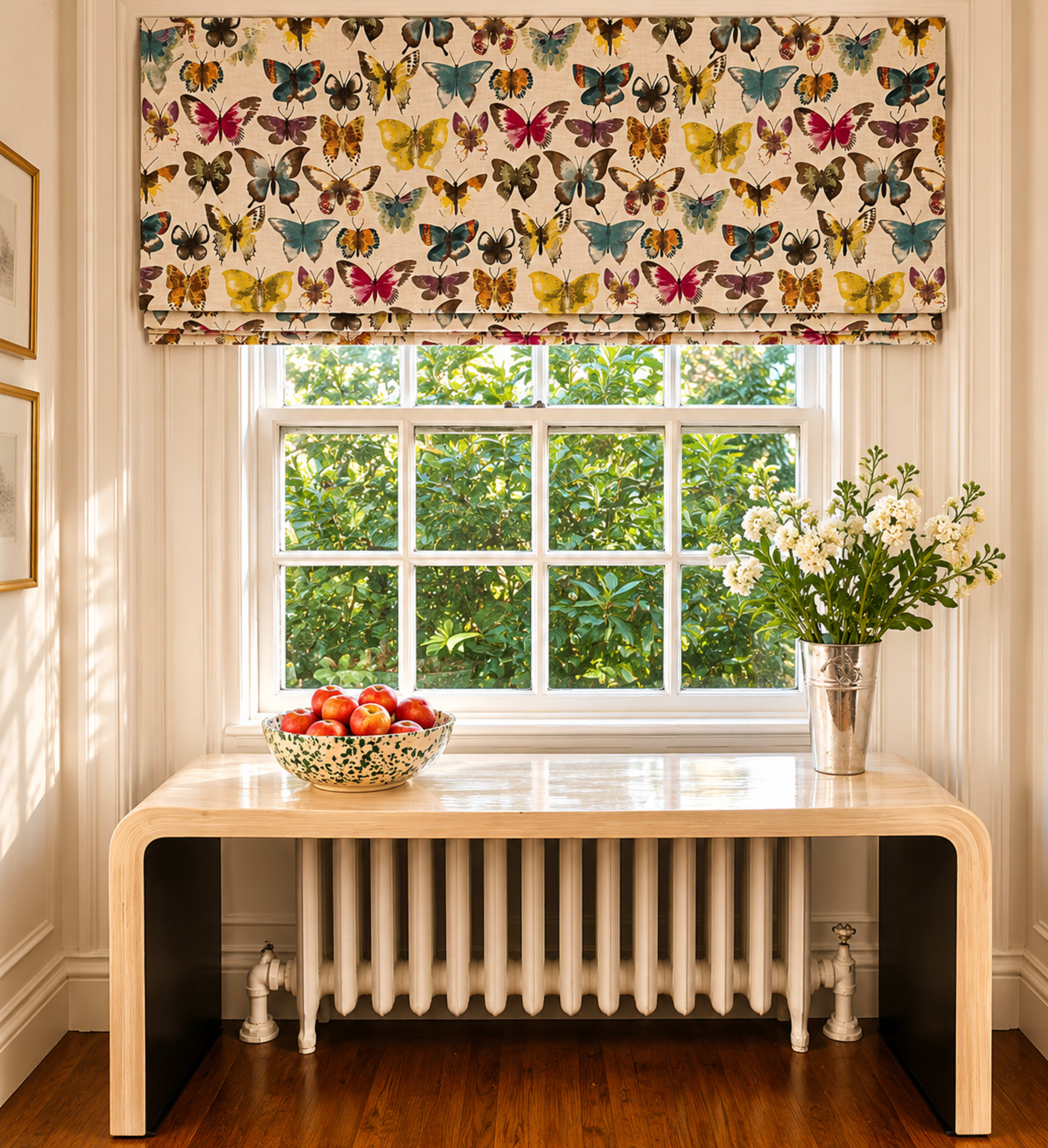 The image shows a bright room with a window dressed in butterfly-patterned fabric, a table with a bowl of apples, and a vase of flowers, all set against a backdrop of greenery outside.