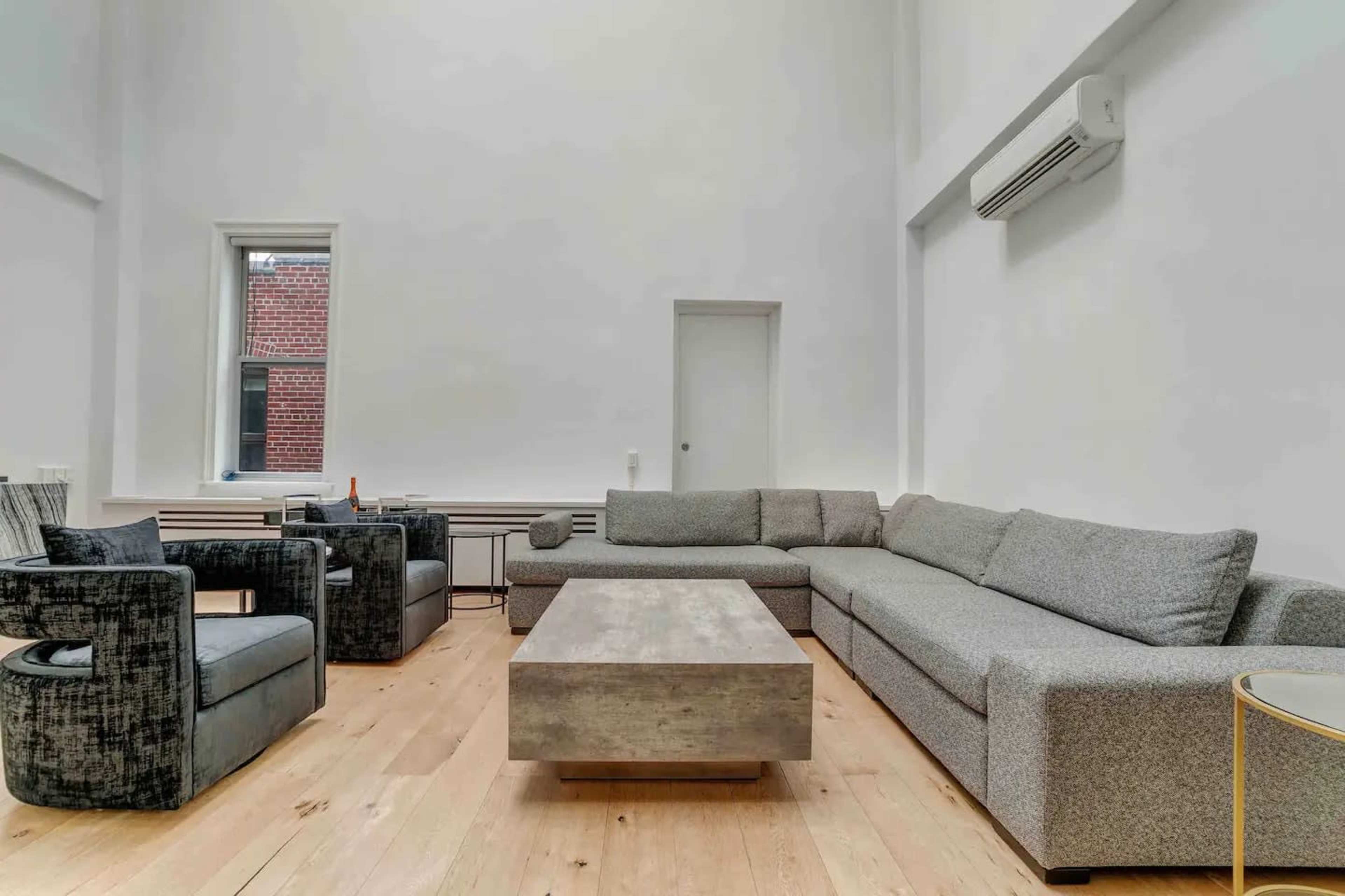 A modern living room with a large grey sectional sofa, two dark armchairs, a rectangular coffee table, and light wooden flooring.