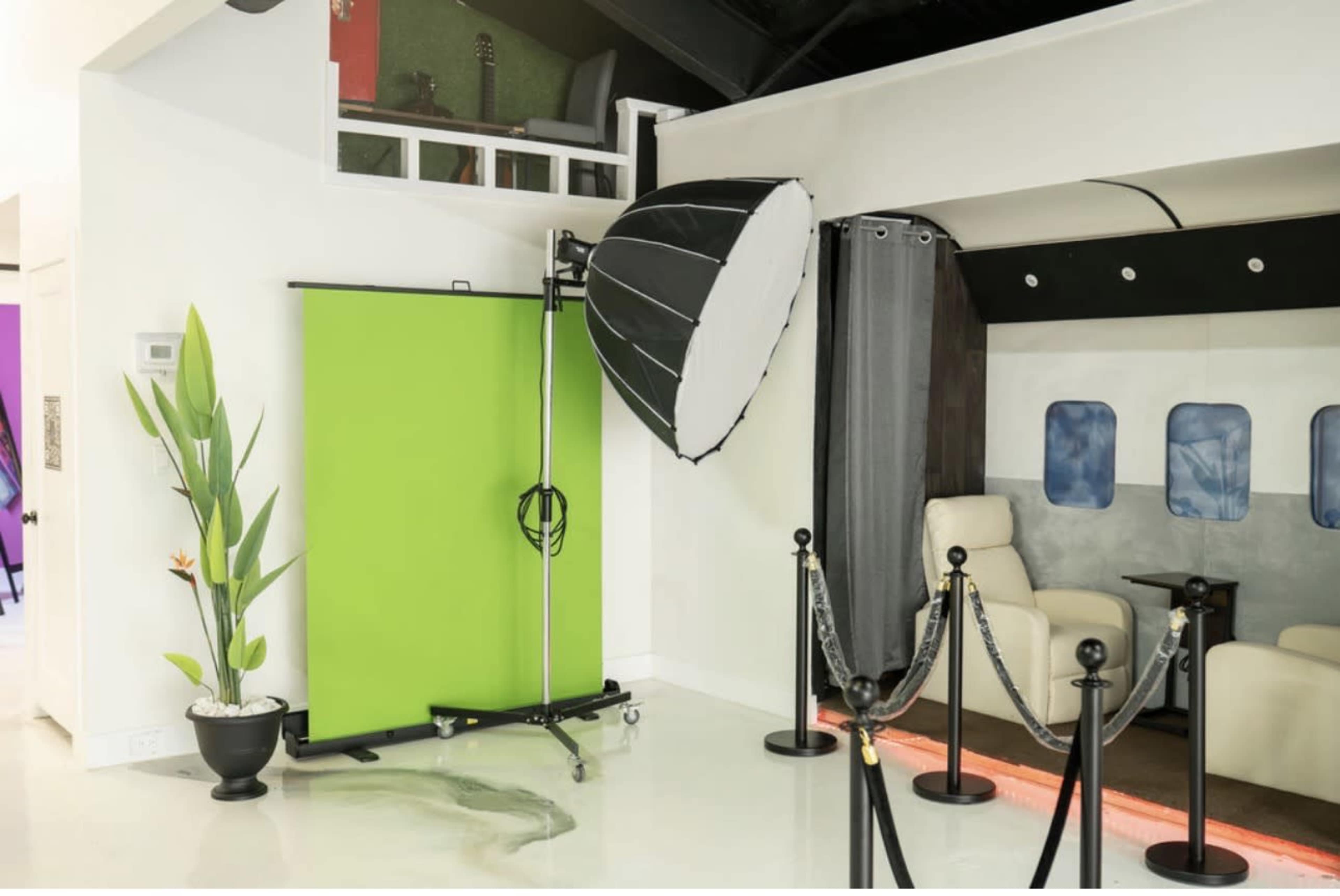 The image shows a photo studio setup featuring a green screen, a large softbox light, and a section designed like an airplane cabin, separated by ropes.