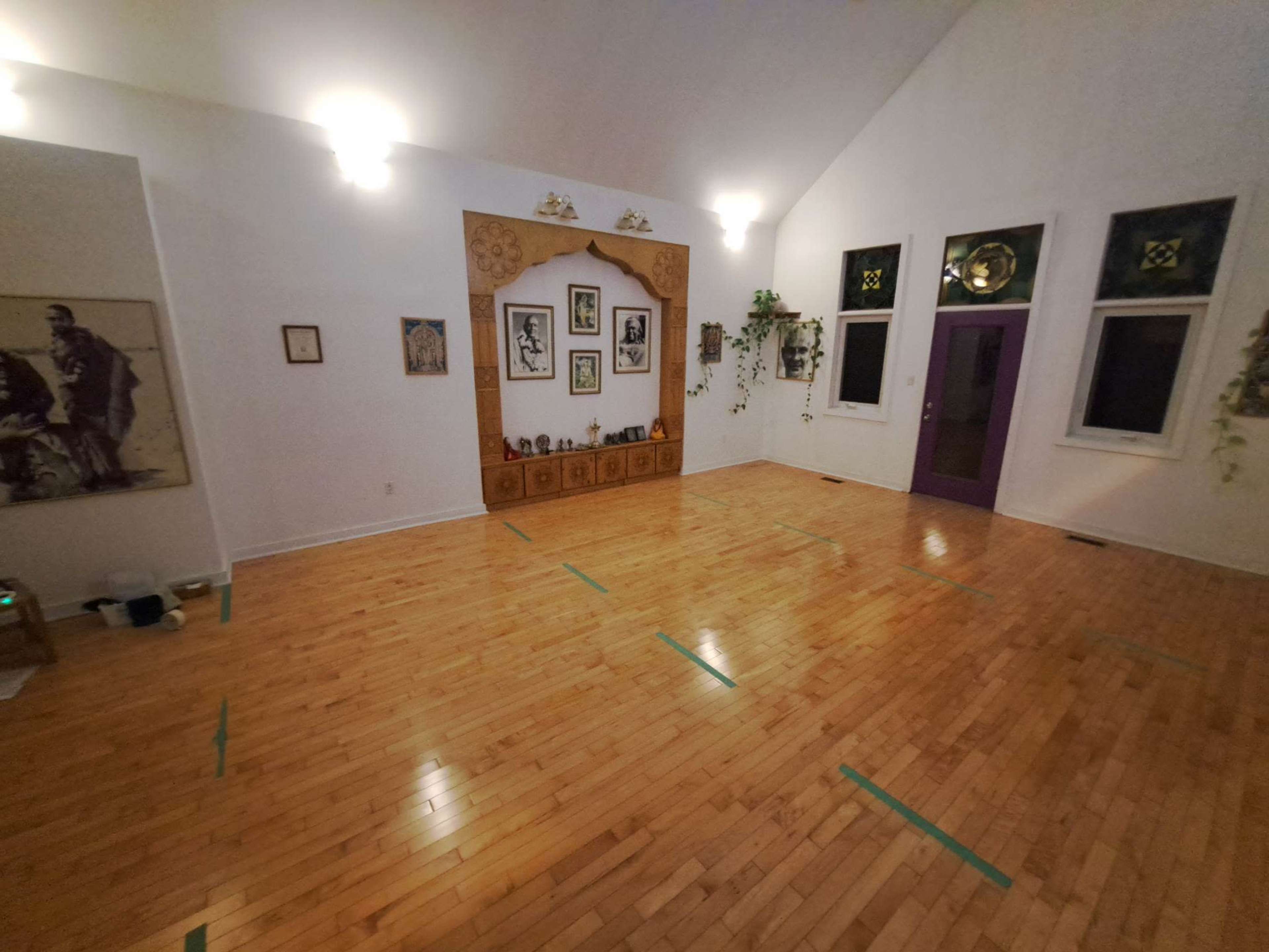 The room features a wooden floor, a decorated wall with framed pictures, and green tape markings on the floor.