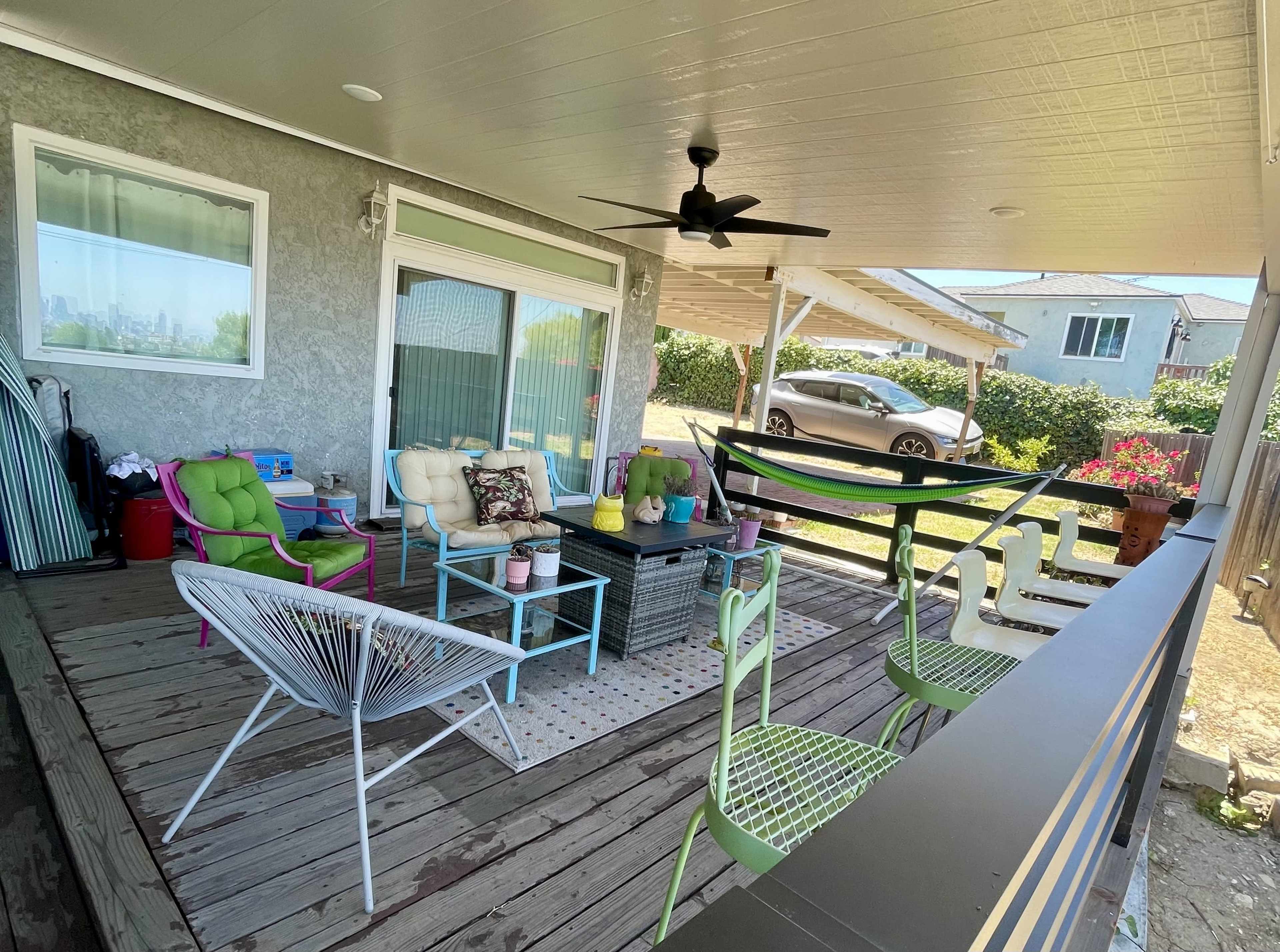 The image shows a covered outdoor patio with various colorful chairs, a coffee table, and a view of a car parked nearby.