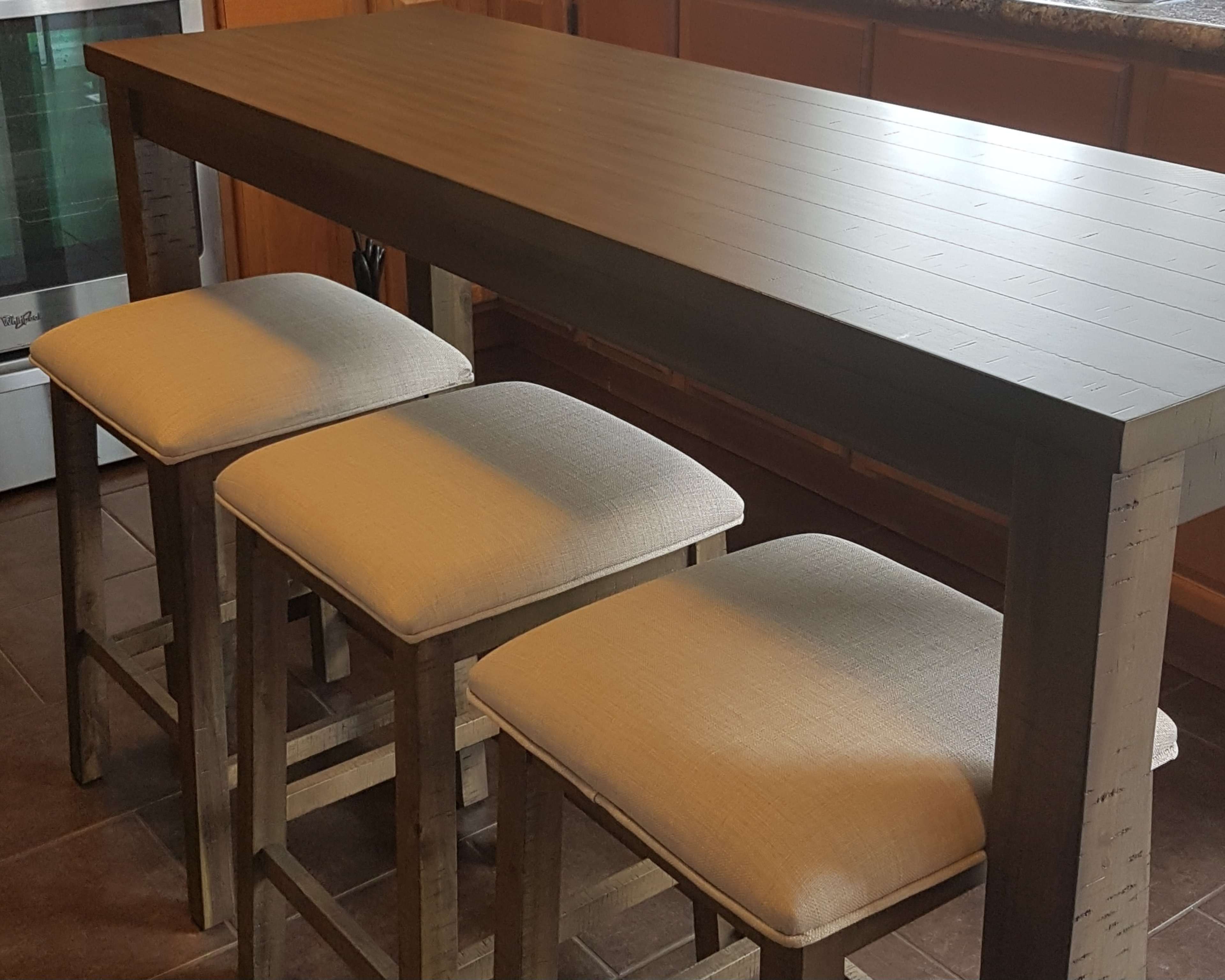 A wooden dining table with a smooth surface and three upholstered stools positioned underneath it.