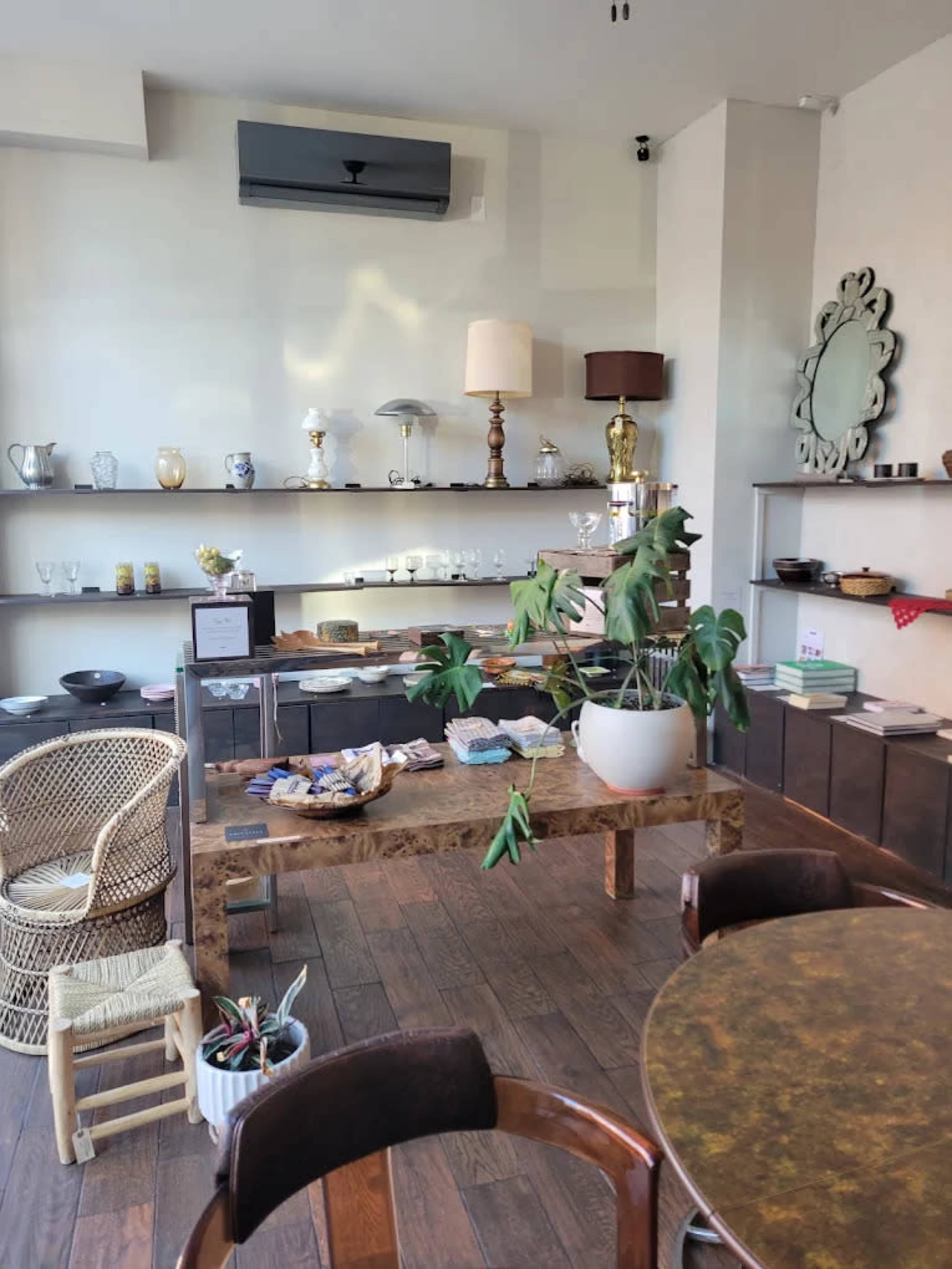The image shows a modern interior of a shop featuring decorative items, a wooden table with products, and a plant in a pot.