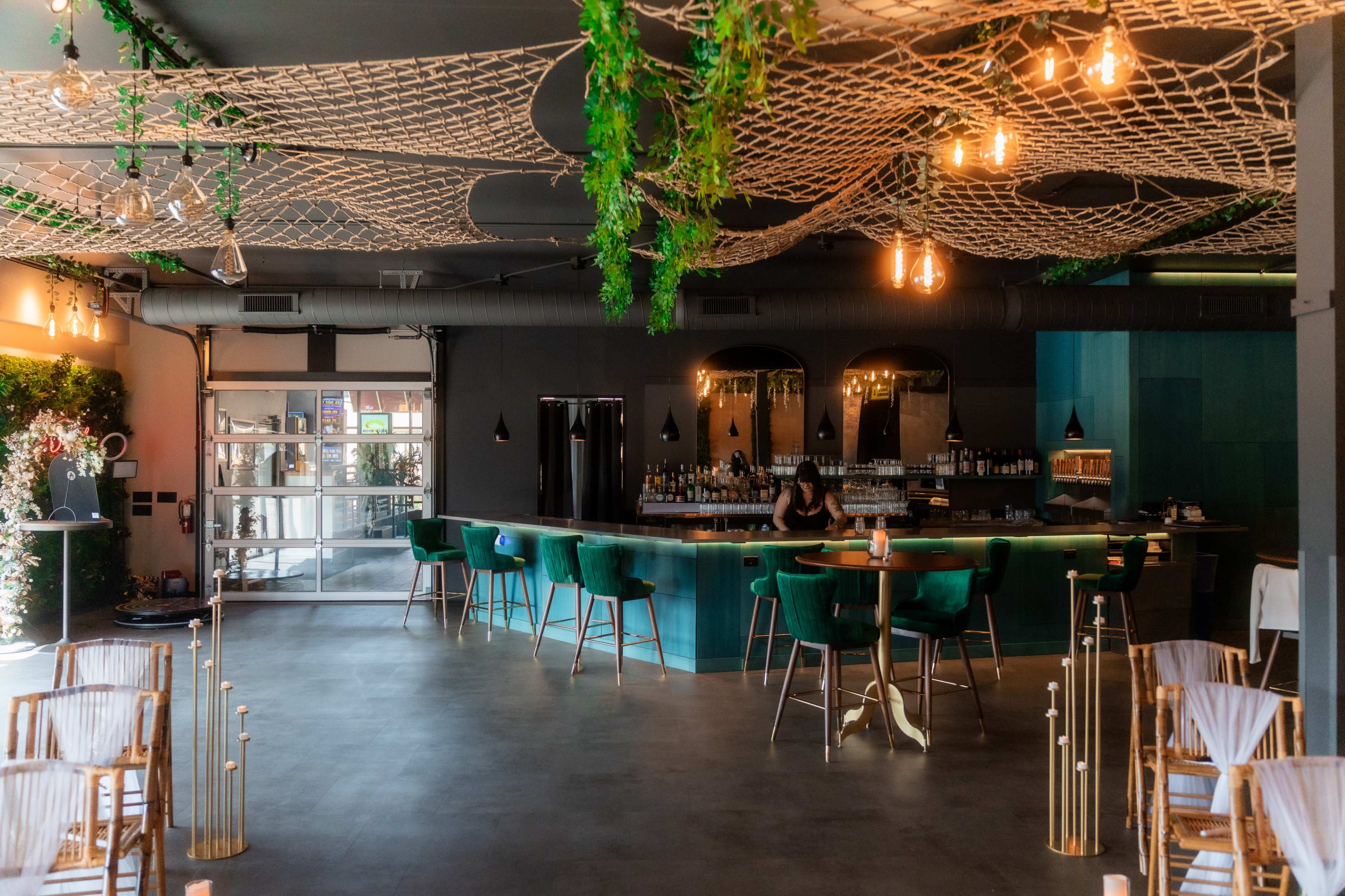 The image shows a modern bar interior with green seating, a large counter, and decorative lighting overhead.