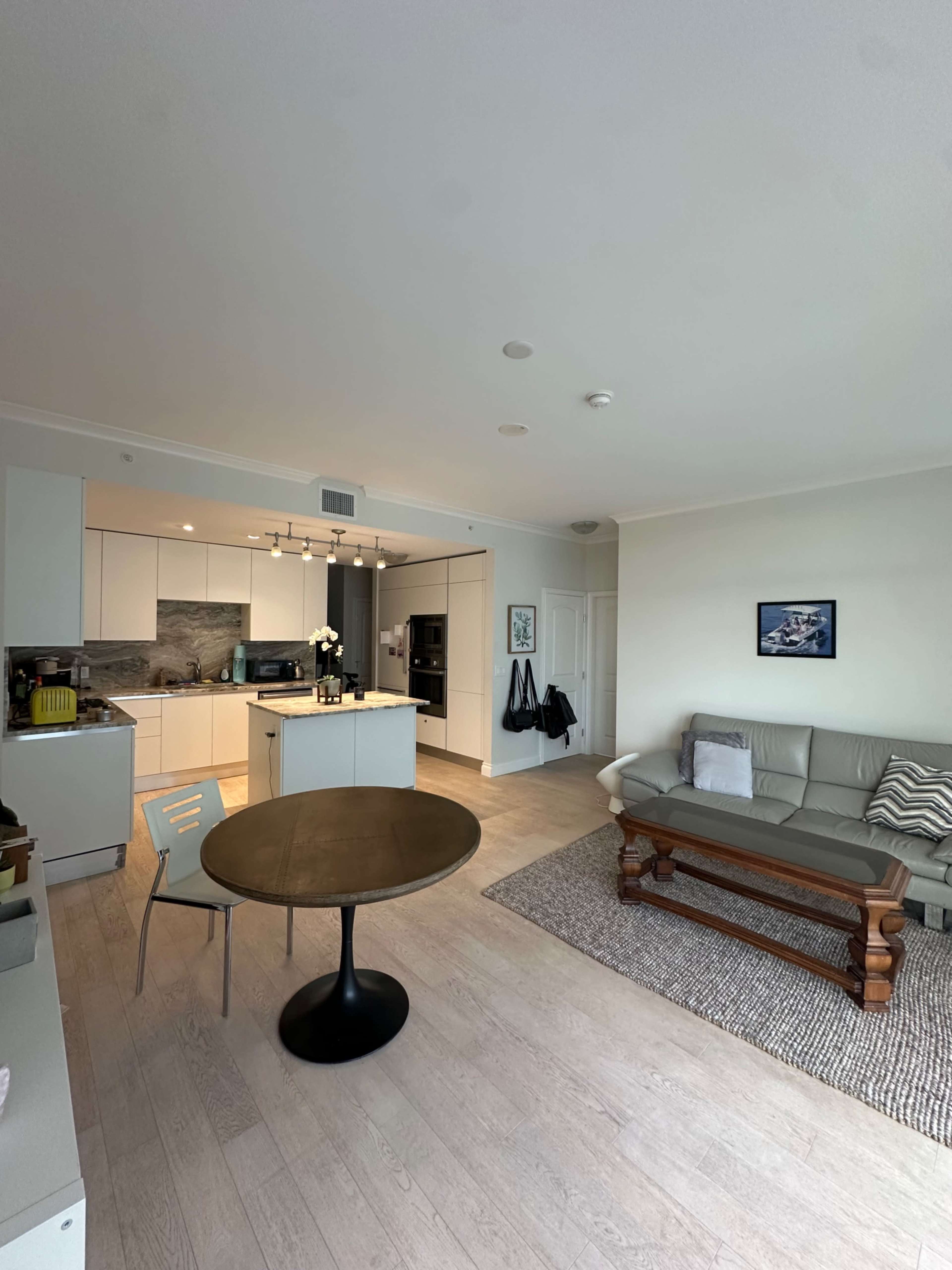 The image shows a modern, open-plan living area featuring a kitchen, dining table, and a seating area with a sofa.