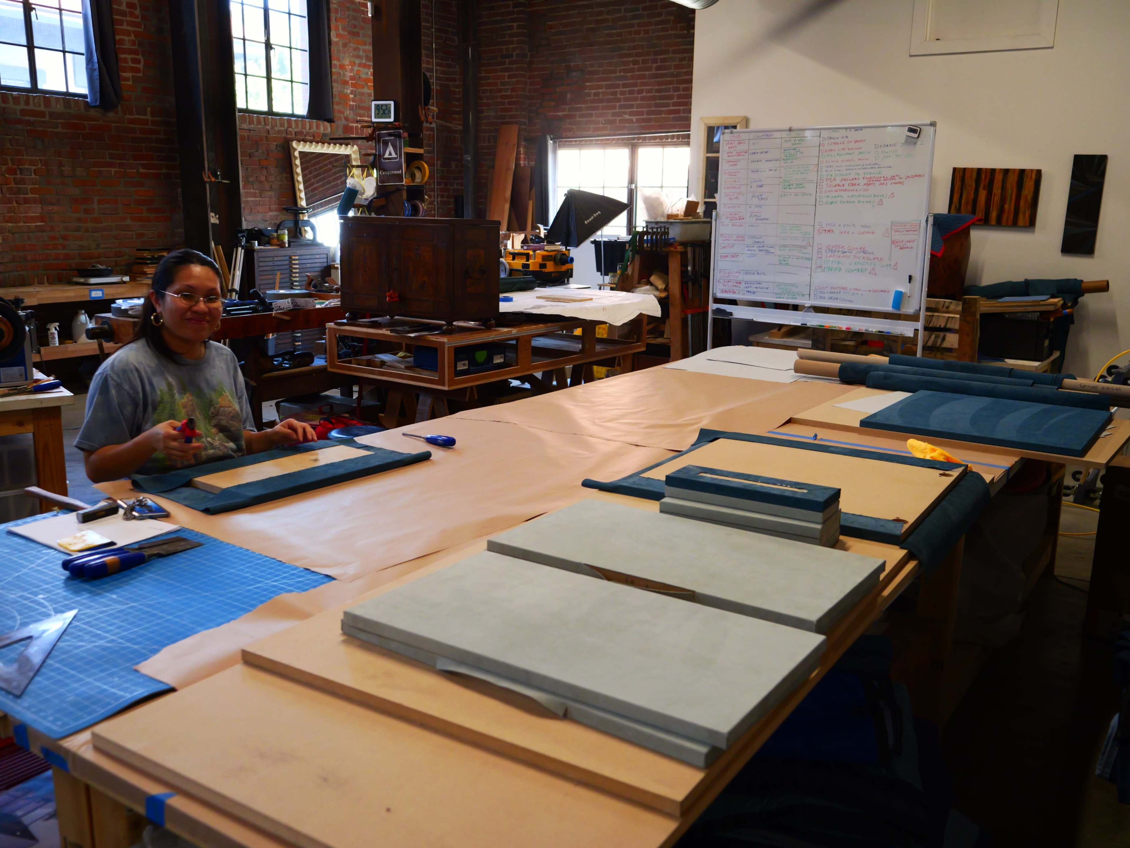 A person is seated at a work table in a workshop, surrounded by various tools and materials.