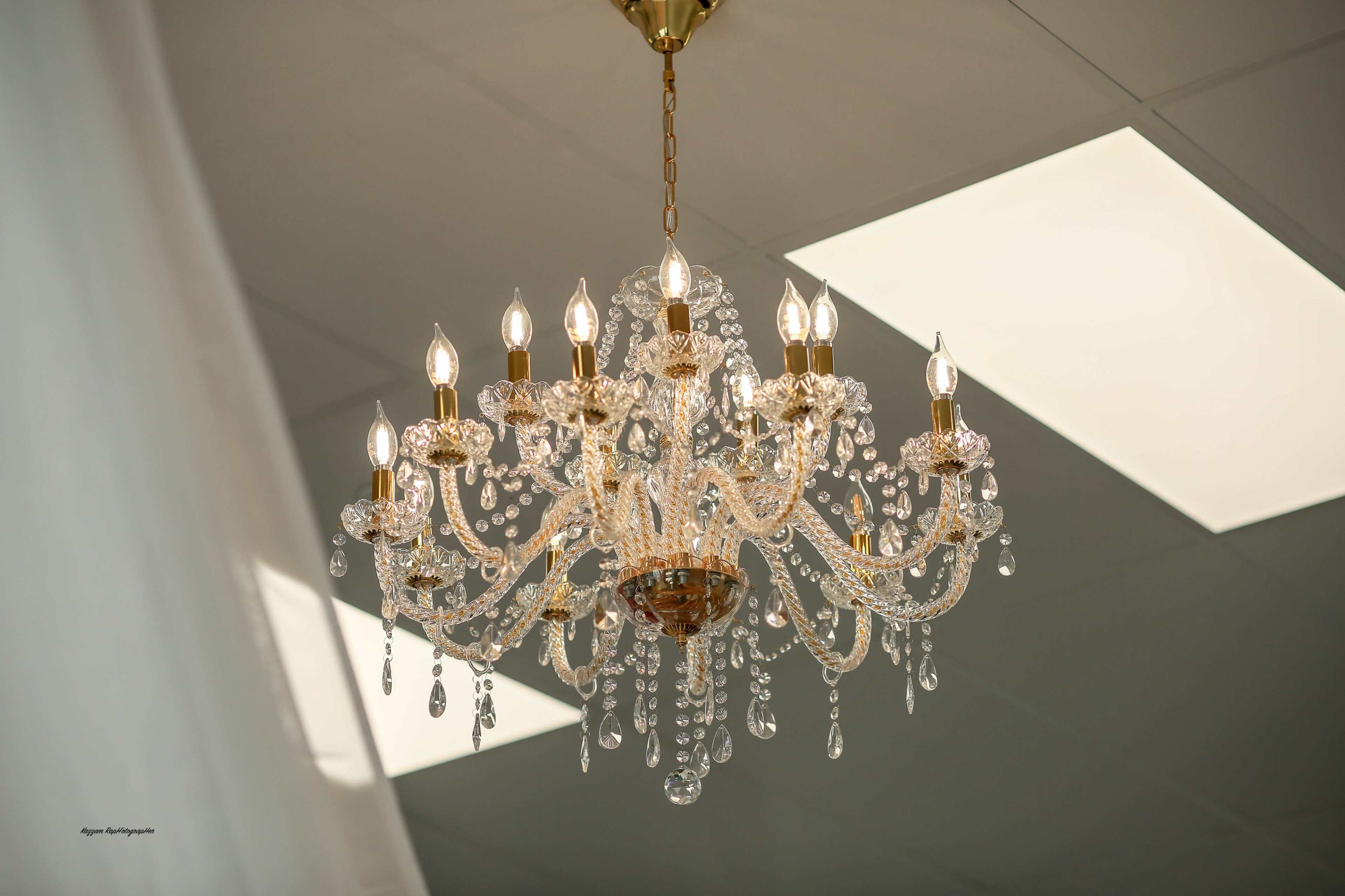 A crystal chandelier with multiple arms and light bulbs hangs from the ceiling in a well-lit room.