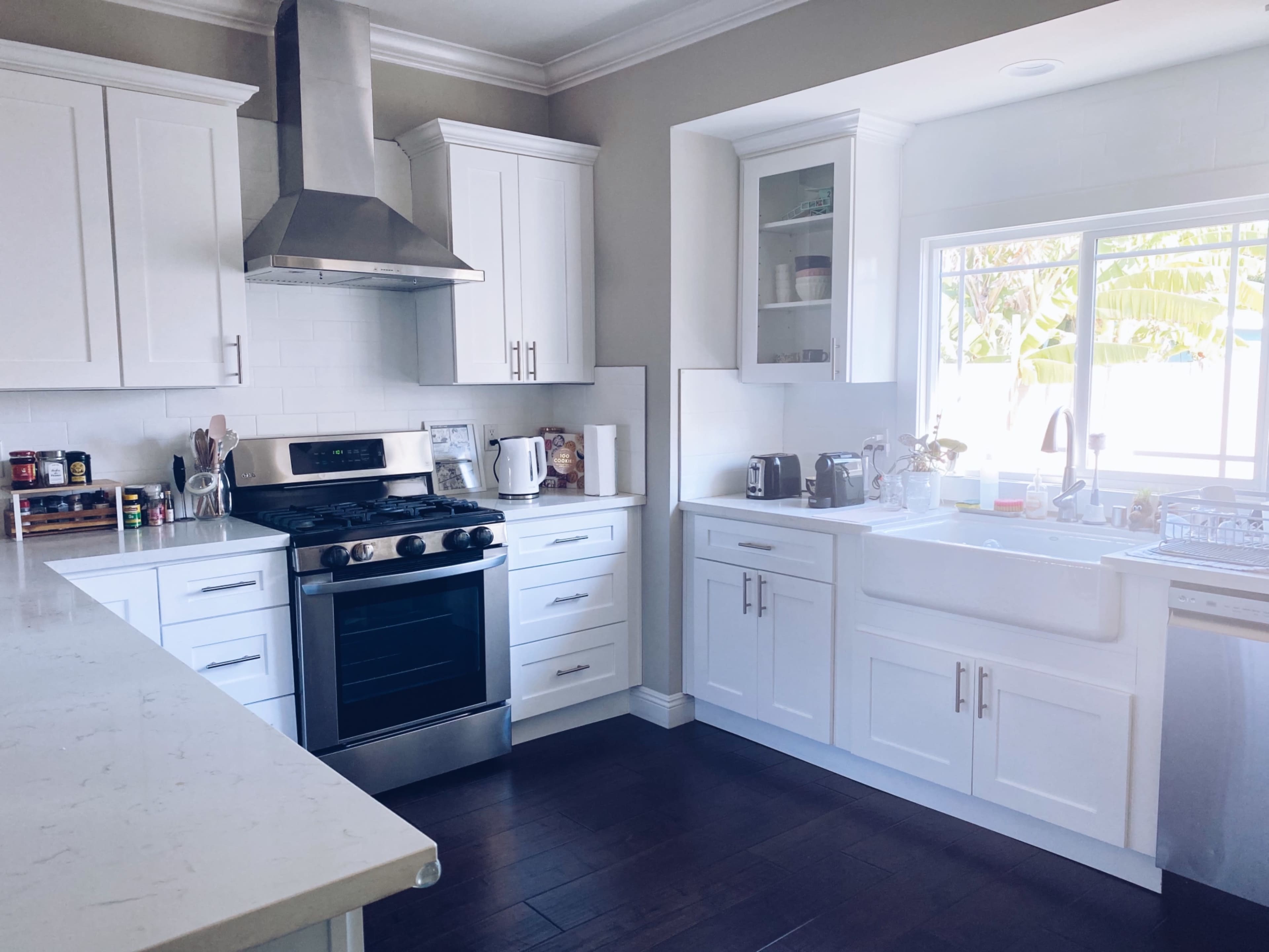 A modern kitchen with white cabinets, stainless steel appliances, and a large sink under a window.